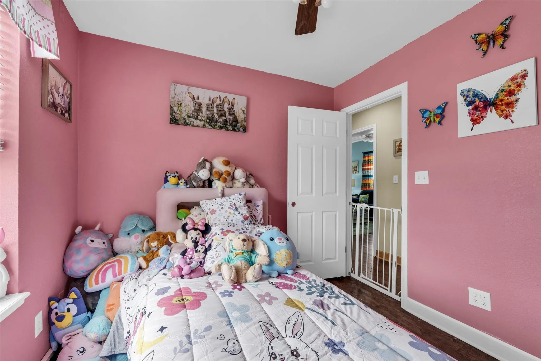 Pink-painted room featuring wood-finish flooring, a white paneled door, and a ceiling fan