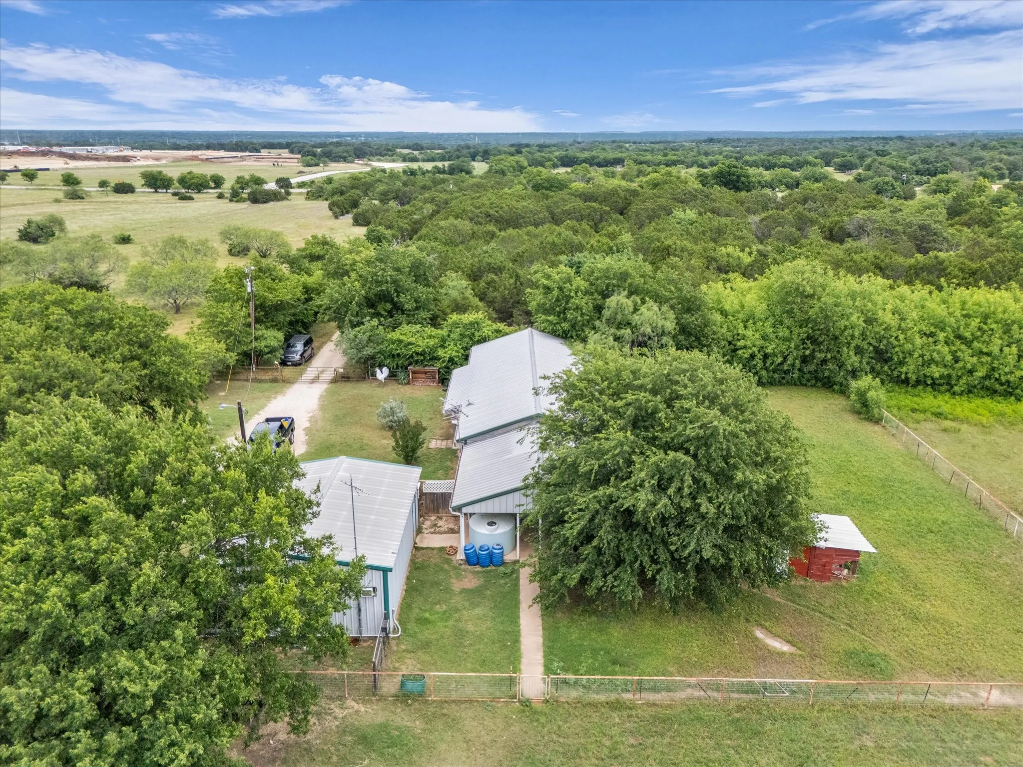 Aerial overview of a property featuring a main structure with a metal roof, a secondary outbuilding, and a red auxiliary shed