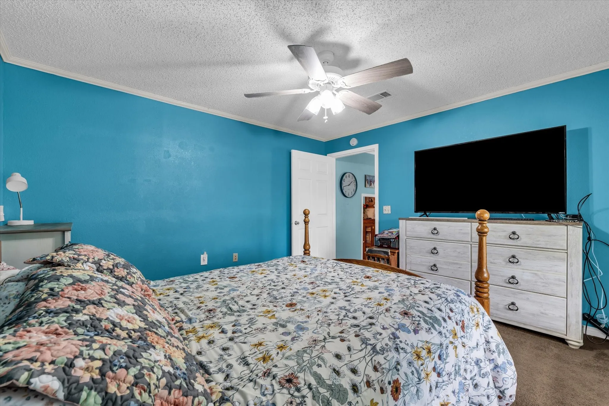 Bedroom featuring a ceiling fan with light fixture, painted walls, crown molding, and carpet flooring