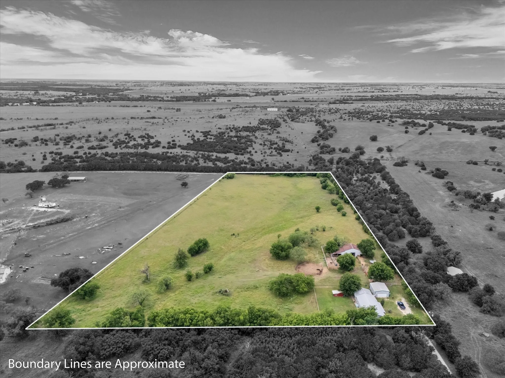 Expansive rural property featuring a large parcel of open land, mature trees, multiple structures, and a perimeter outlined by white boundary lines