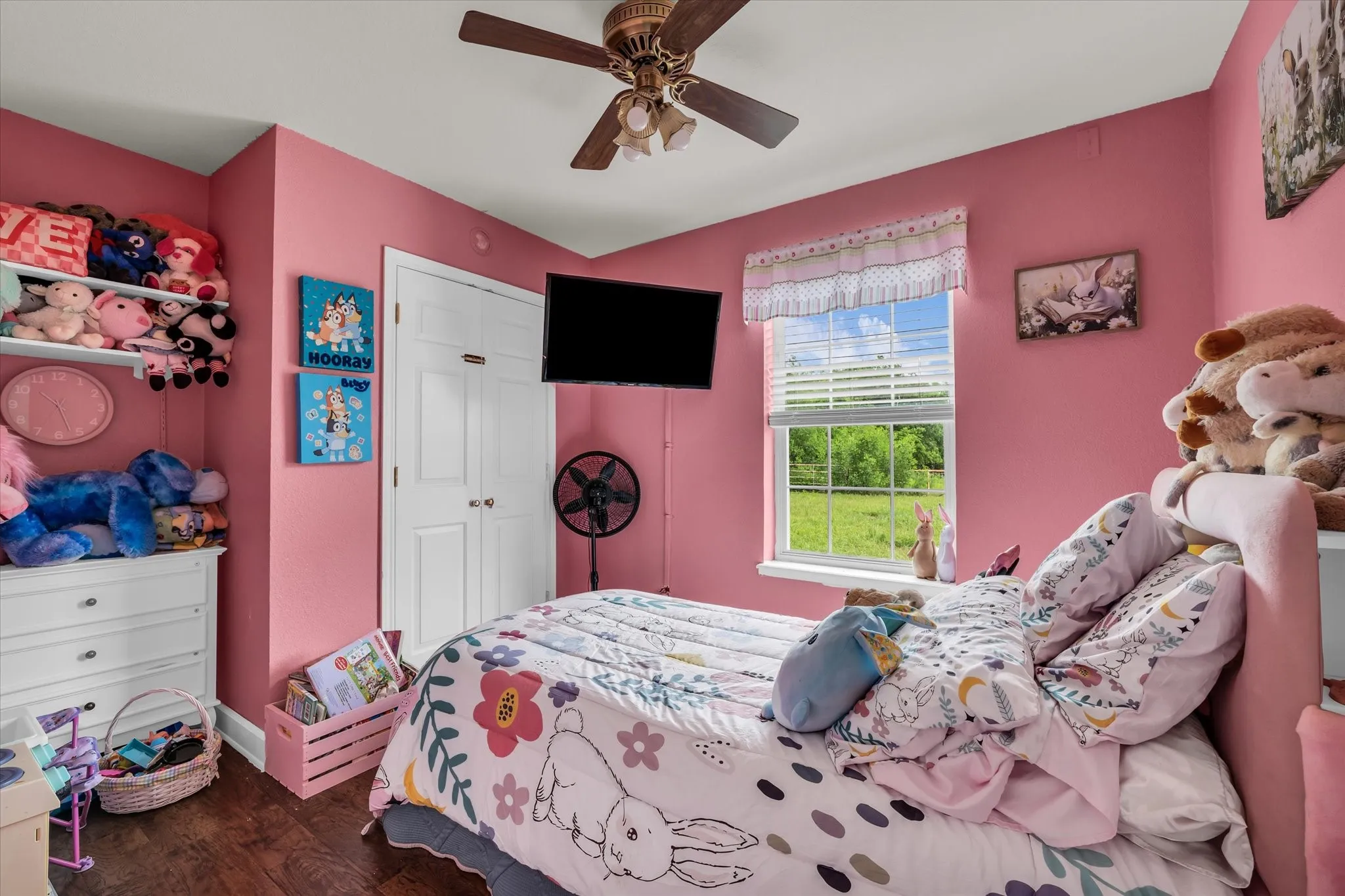 Interior room featuring wood-finish flooring, a ceiling fan, a window with blinds, and white bi-fold doors