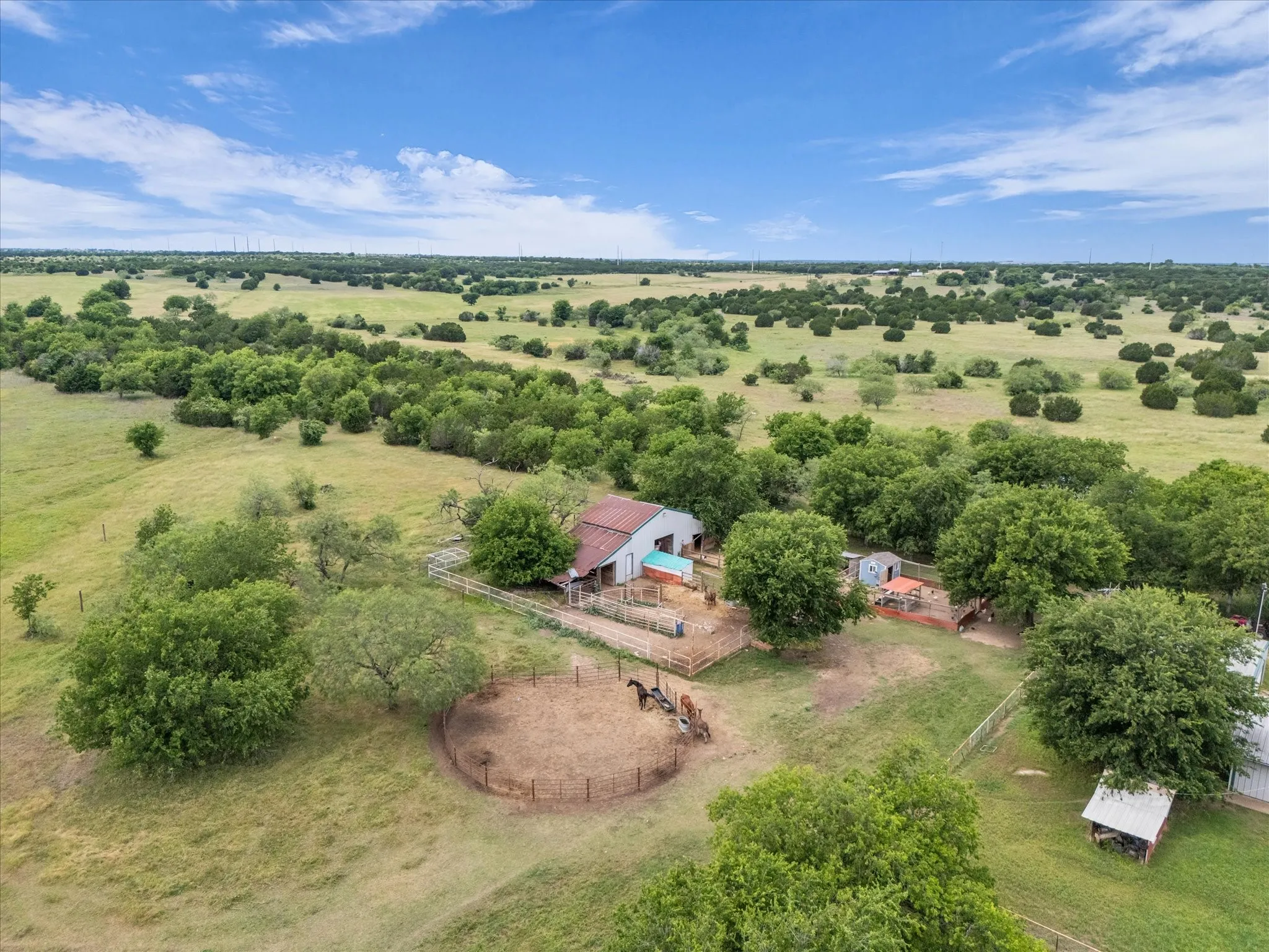 Expansive pastoral acreage featuring scattered trees, a barn with an attached fenced enclosure, and a round pen