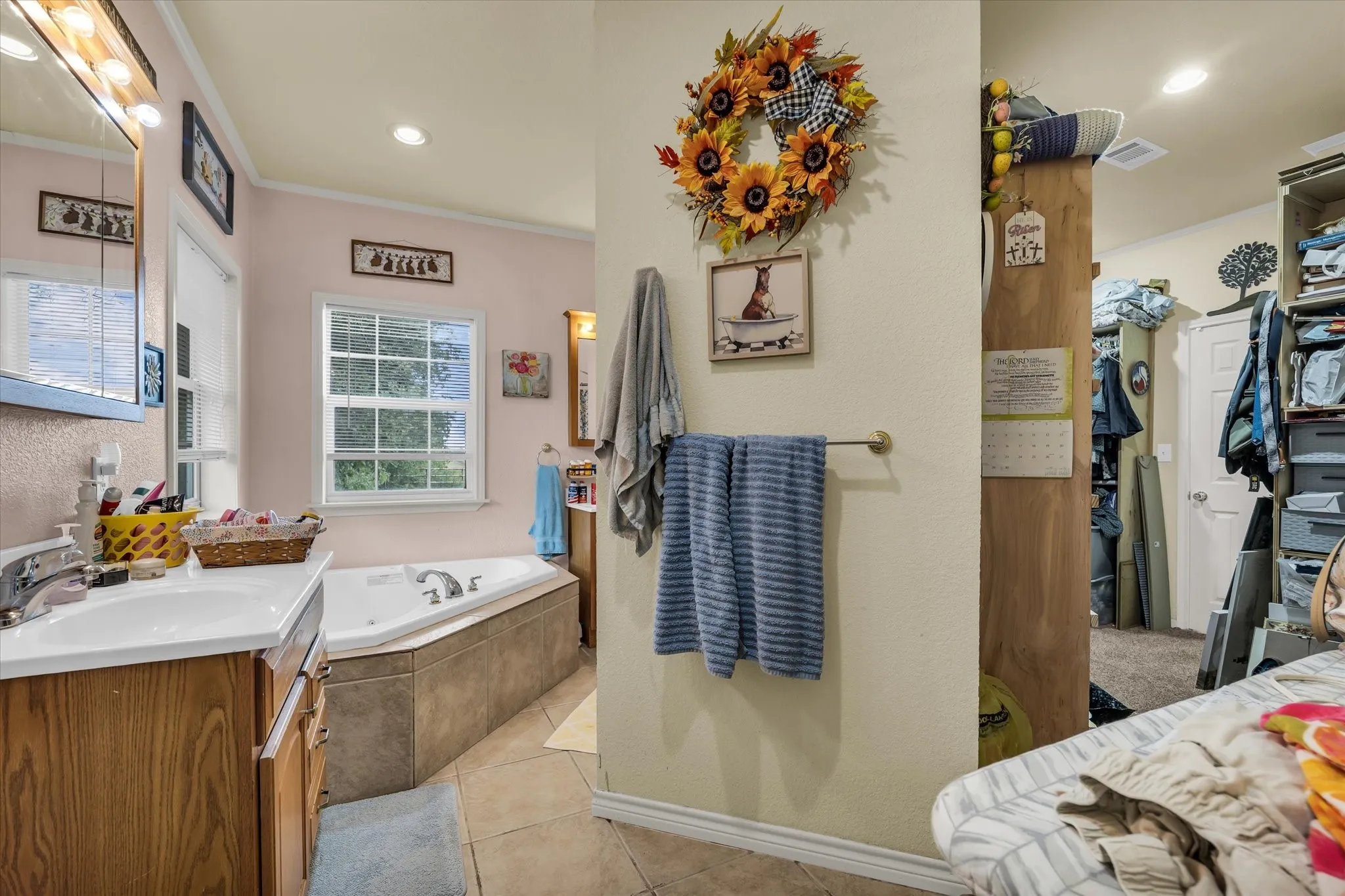 Bathroom featuring a built-in jetted tub with tiled surround, wood-finish vanity with an integrated sink, and tiled flooring