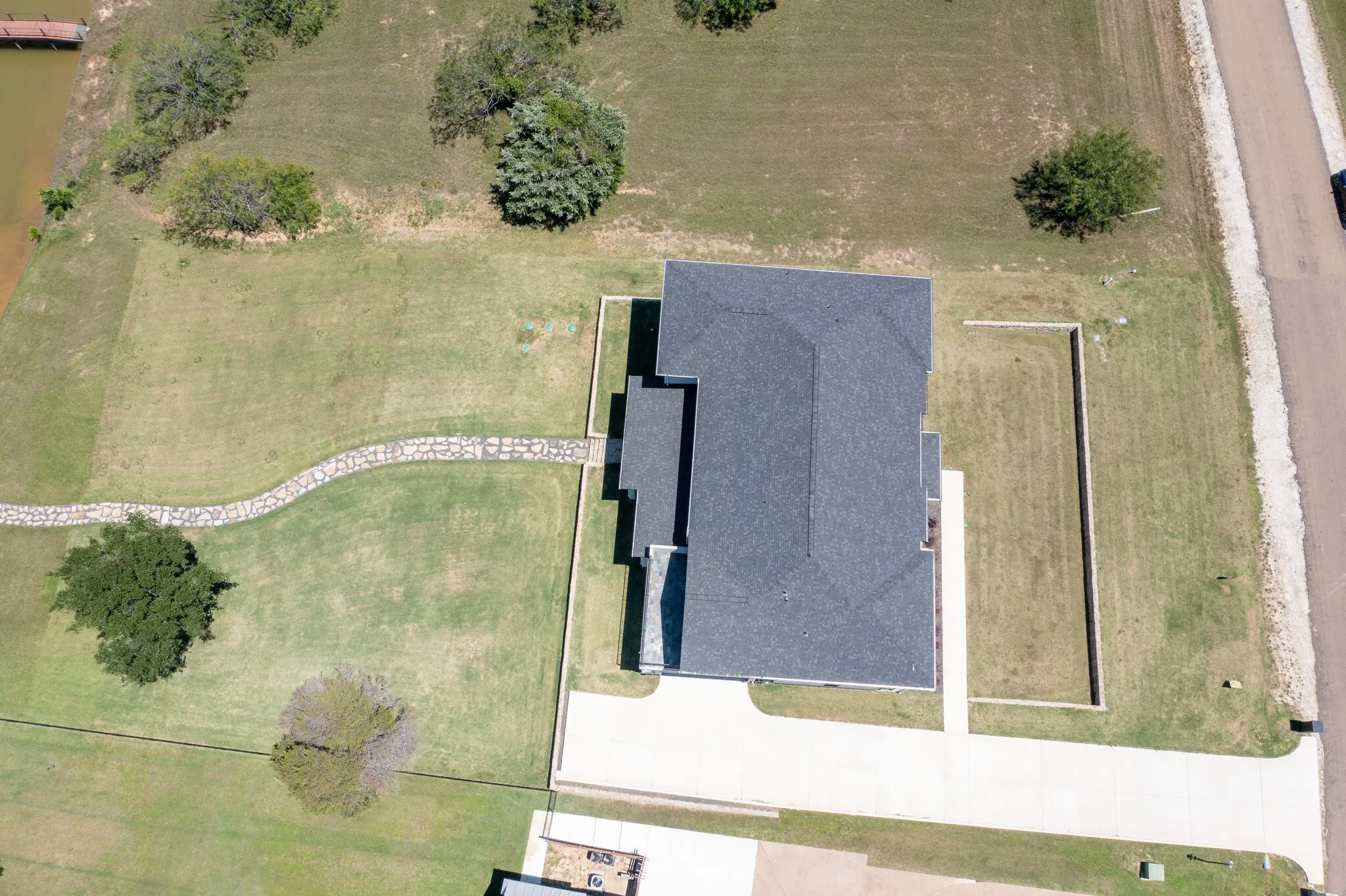 New construction residence featuring a dark shingle roof, a concrete driveway, and a stone-lined pathway