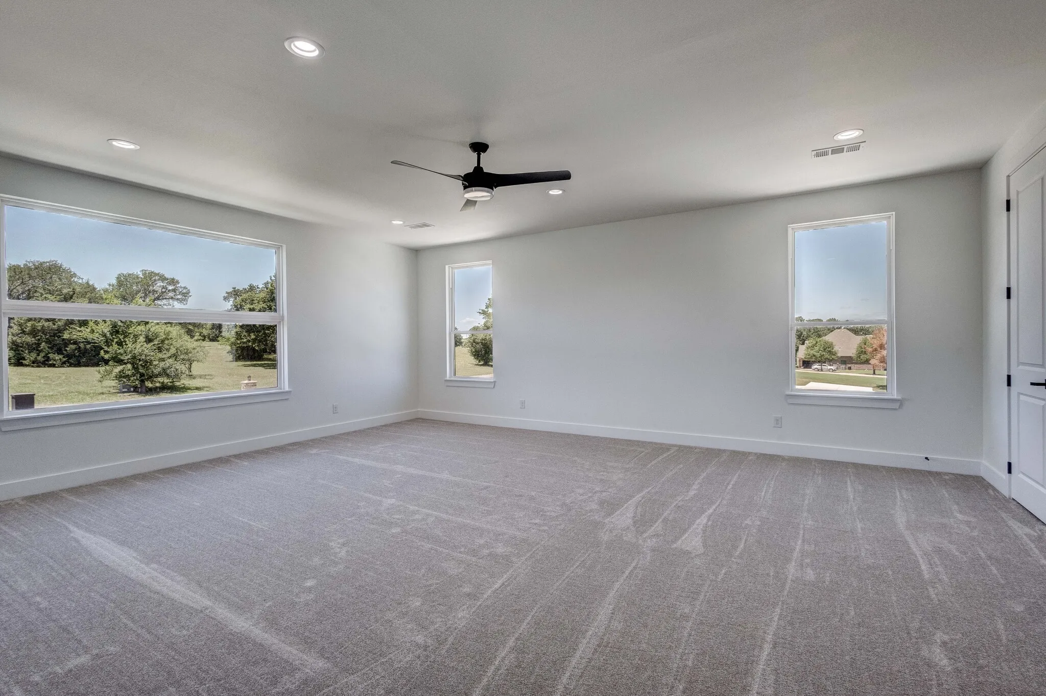 Spacious room featuring neutral carpeting, a contemporary ceiling fan, and multiple windows