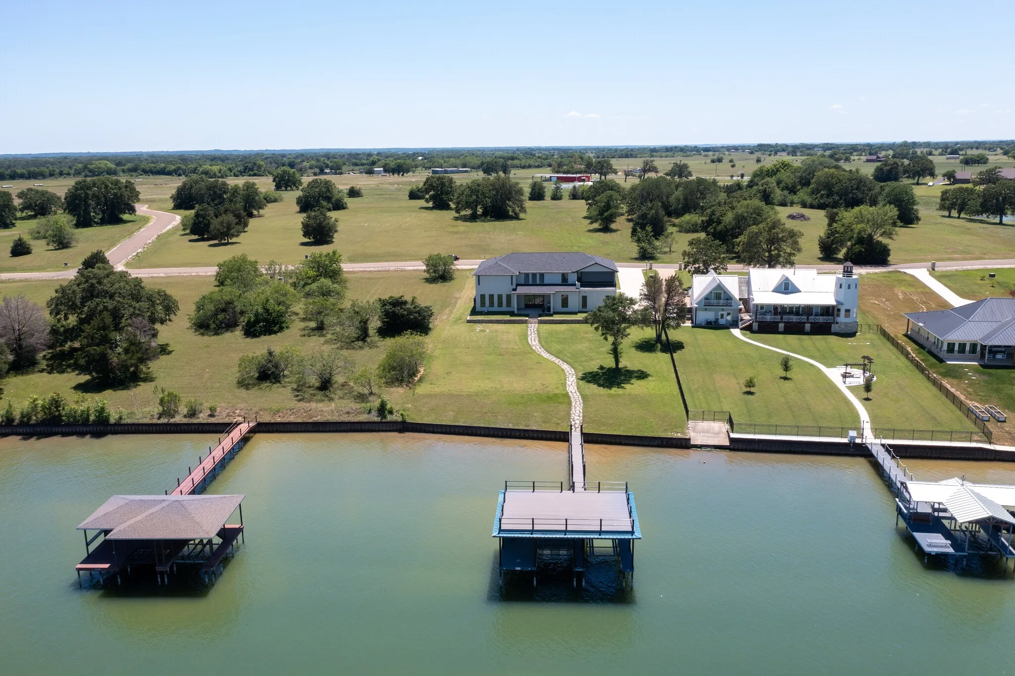 Waterfront property featuring a private boat dock with a covered slip, a multi-story residence with a lighthouse-style architectural element, a stone pathway, a manicured lawn, and a secondary dock