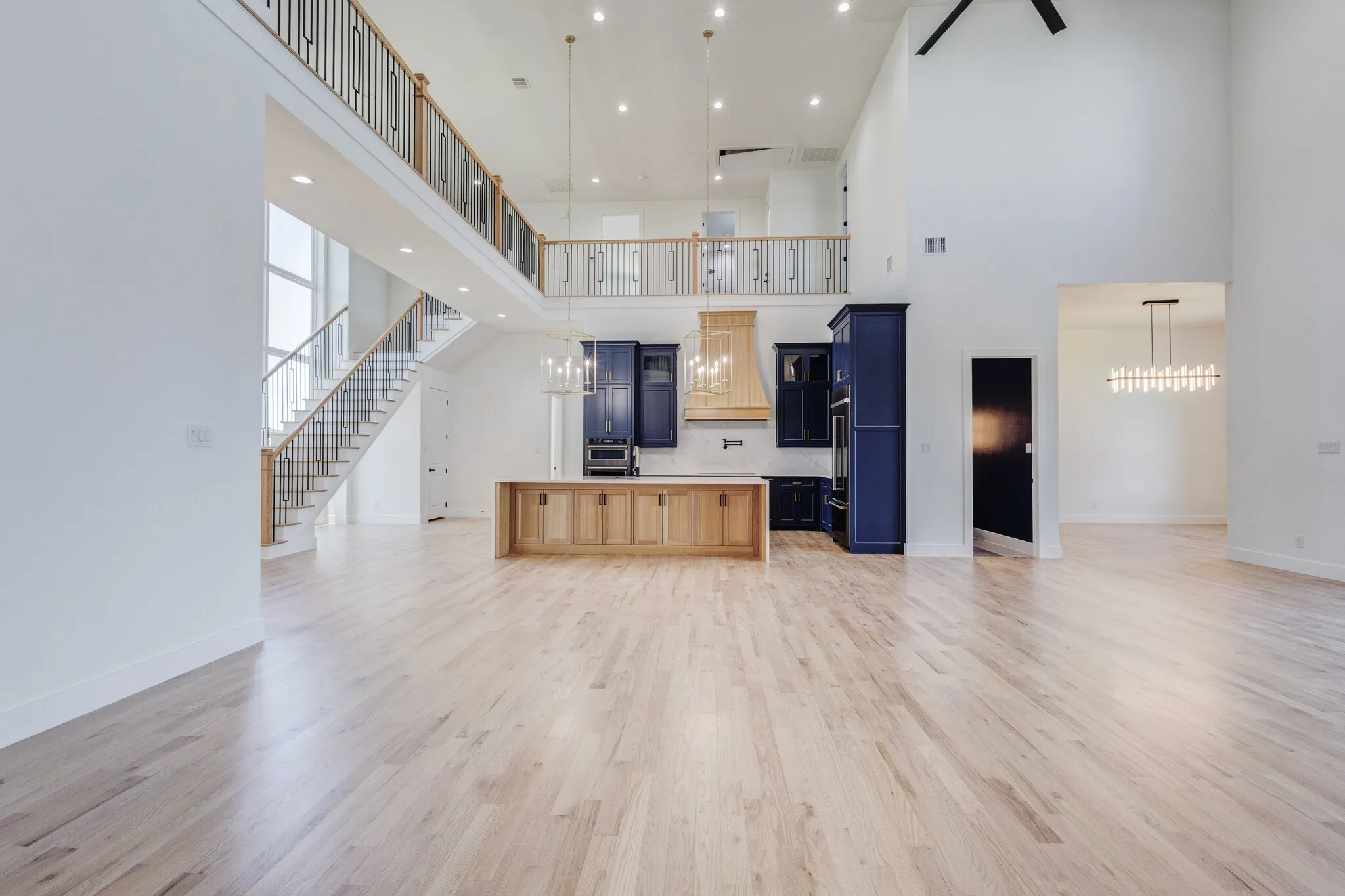 Expansive great room featuring light wood-finish flooring, a two-story ceiling, and a prominent staircase with a wrought iron railing