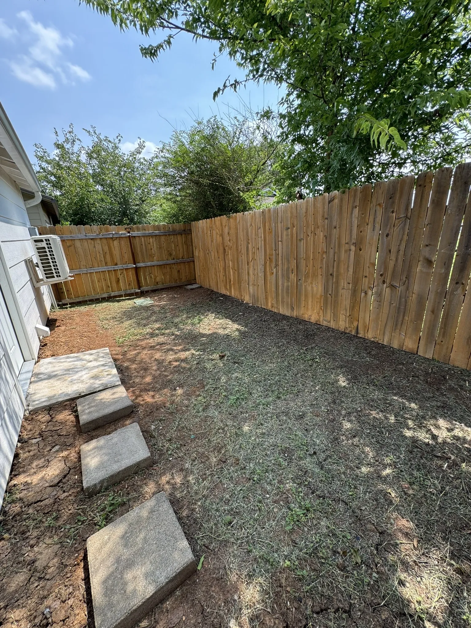 Compact outdoor space featuring a new wood fence, a section of concrete stepping stones, and an area prepared for landscaping