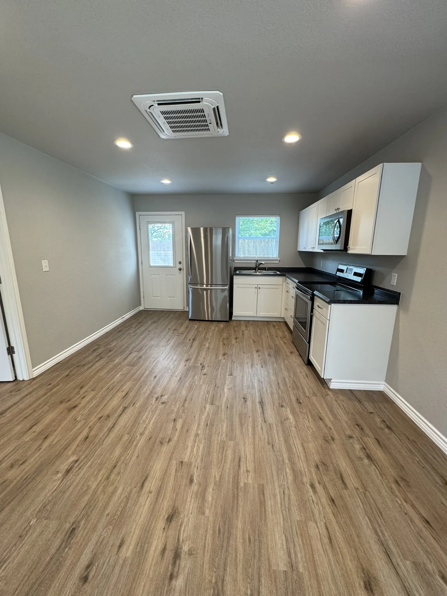Spacious kitchen and living area featuring wood-finish flooring, recessed lighting, and a white paneled exterior door