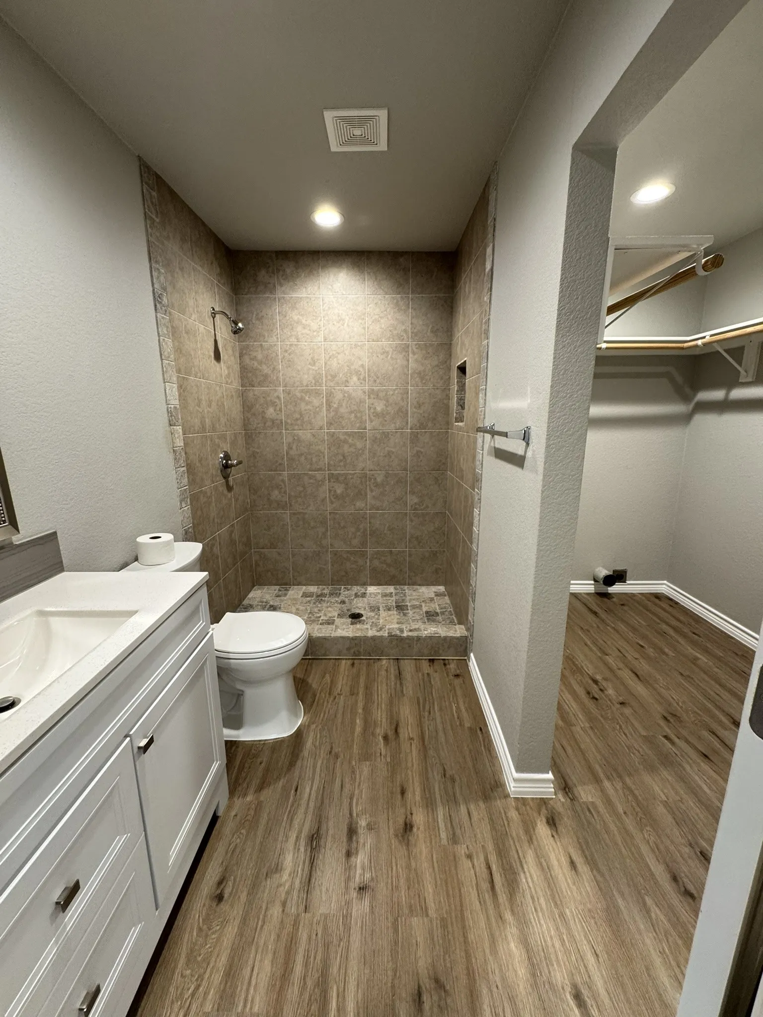 Three-piece bathroom featuring a walk-in shower with tiled walls and floor, a white toilet, and a vanity with an integrated sink