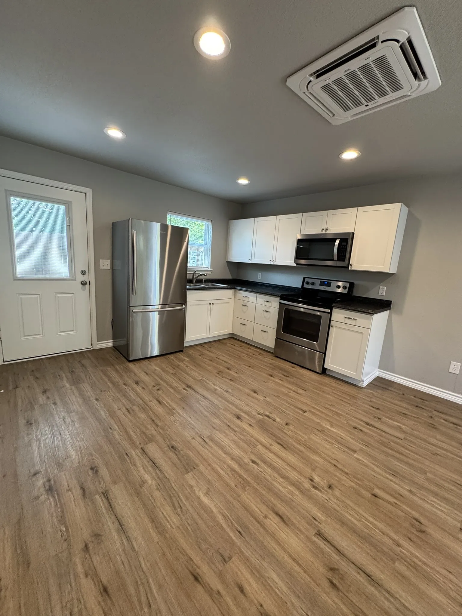 Kitchen area featuring wood-finish flooring, white cabinetry with dark countertops, stainless steel appliances, and recessed lighting