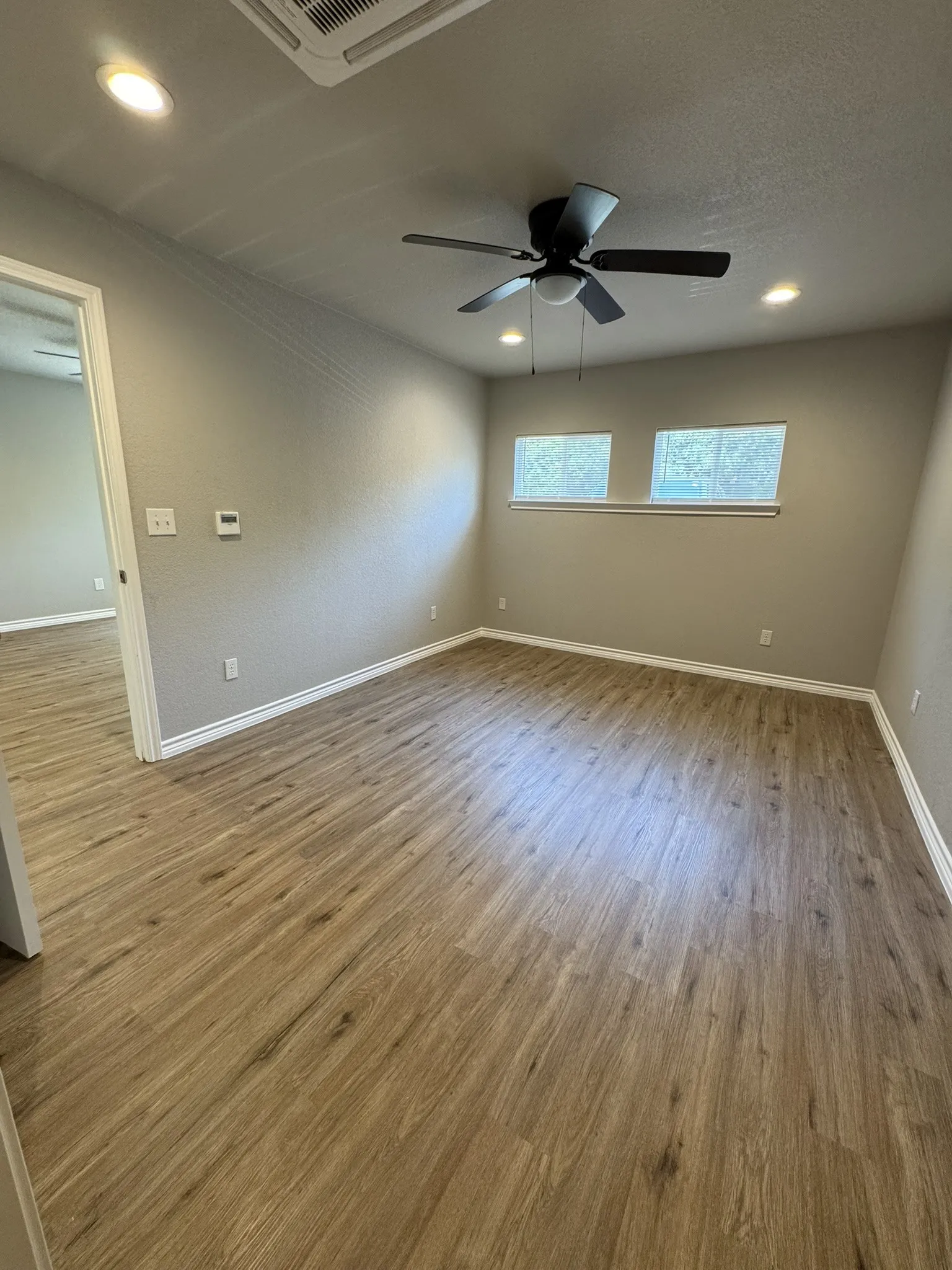 Spacious room featuring wood-finish flooring, recessed lighting, a ceiling fan, and multiple windows