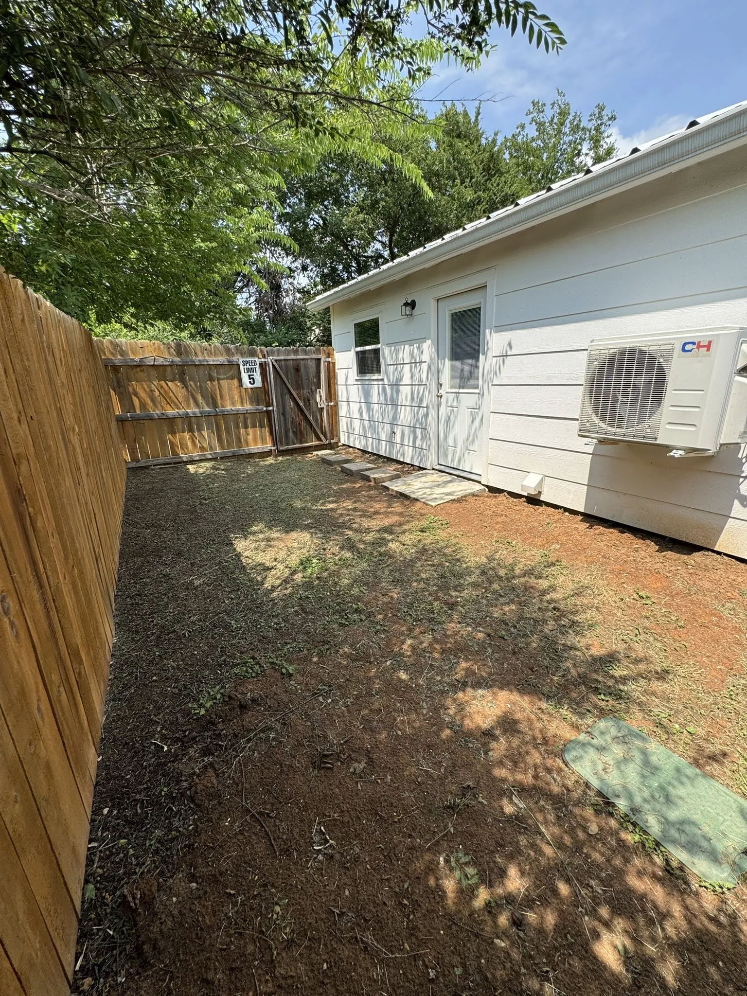 Private backyard space featuring wood fencing, a dedicated entry door, a window, and an exterior mini-split unit