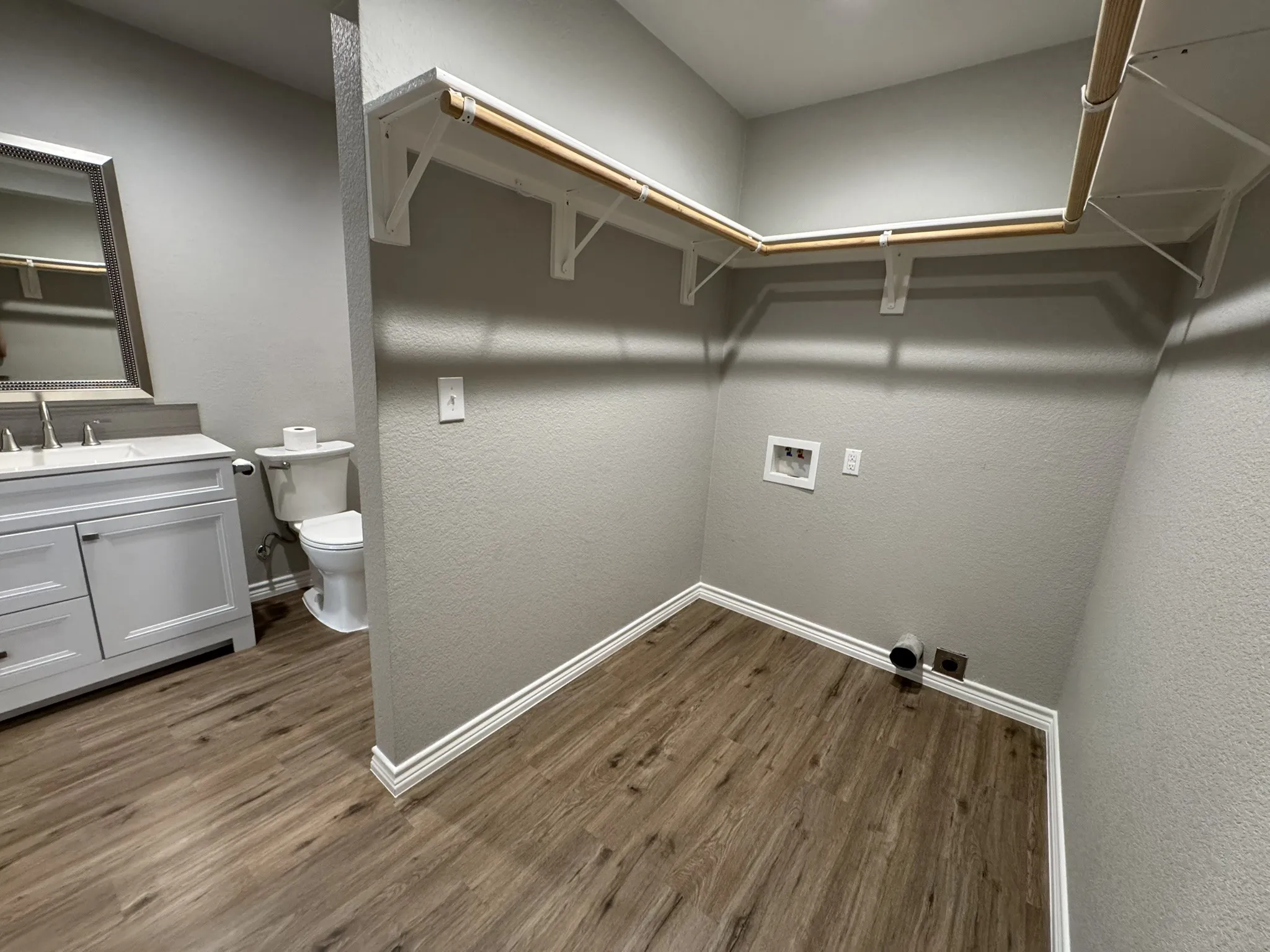 Utility area featuring wood-finish flooring, white baseboards, and built-in shelving with hanging​​‌​​​​‌​​‌‌​‌‌​​​‌‌​‌​‌​‌​​​‌​​ rods