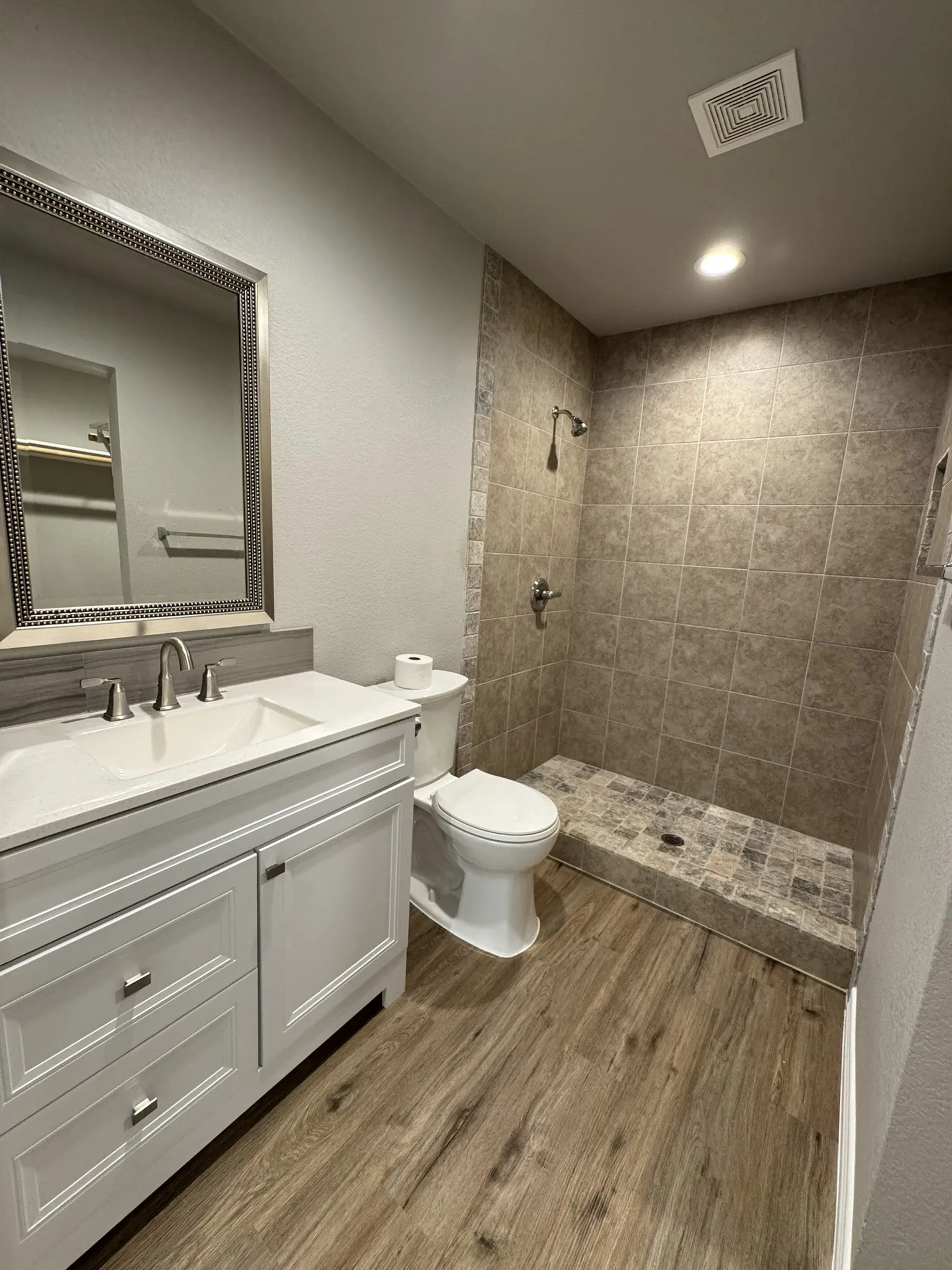 Contemporary bathroom featuring a walk-in shower with tile surround, a white vanity with an integrated sink, polished chrome fixtures, and wood-finish flooring