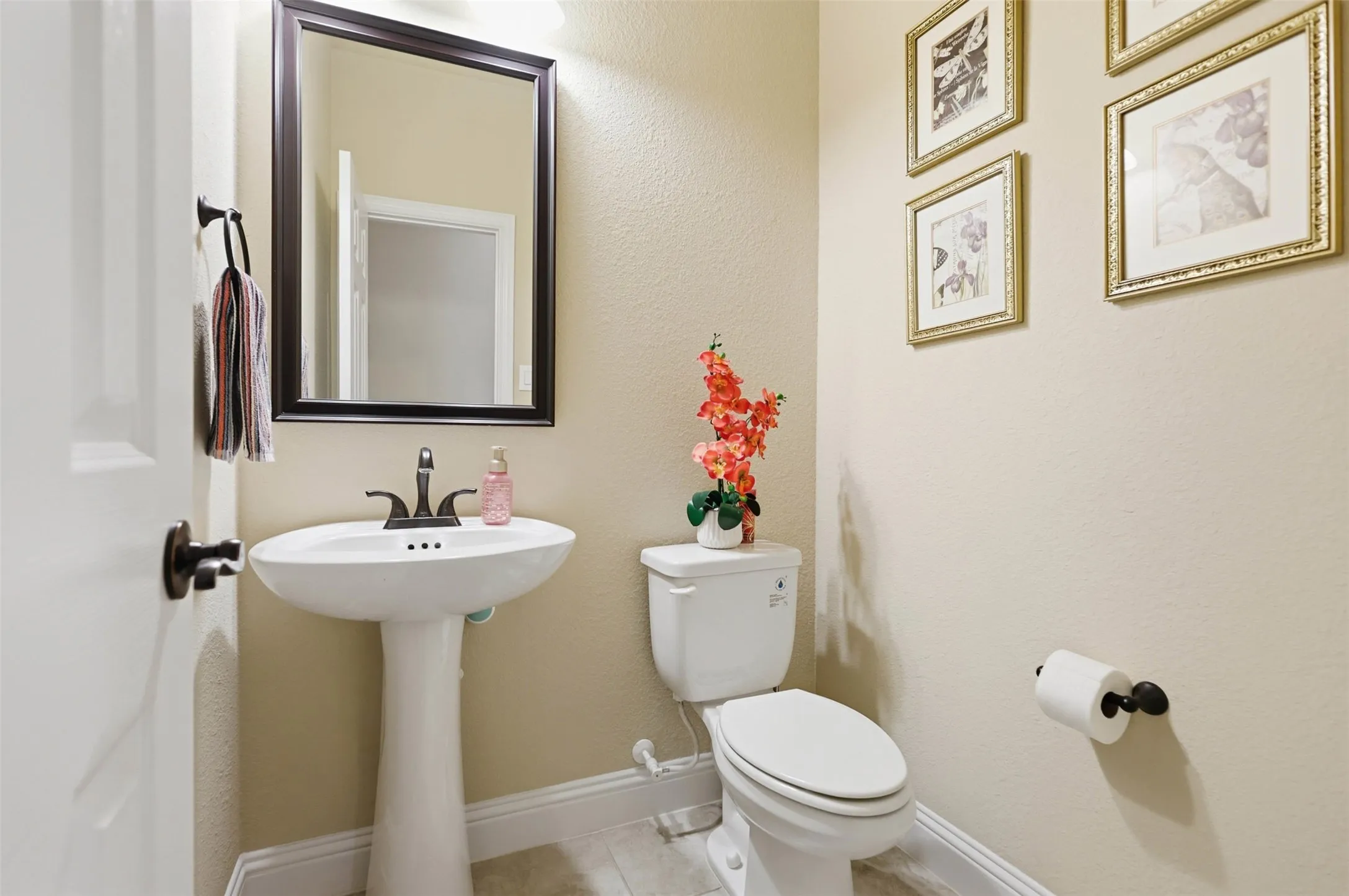 Pedestal sink with dark bronze faucet, framed mirror, and built-in toilet