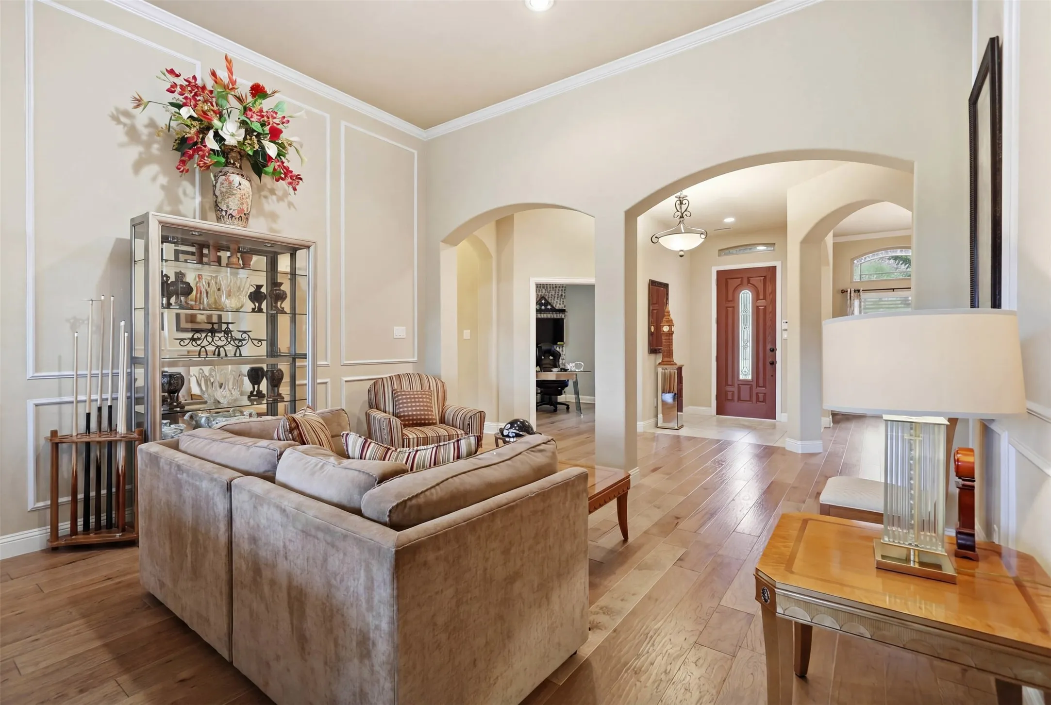 Spacious living area featuring wood-finish flooring, arched doorways, a coffered ceiling with crown molding, and decorative wall paneling