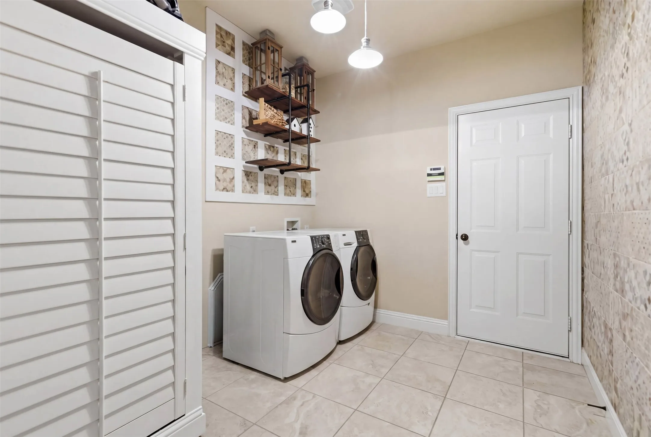 Laundry area featuring large format floor tiling, a white paneled door, and built-in white louvered cabinetry