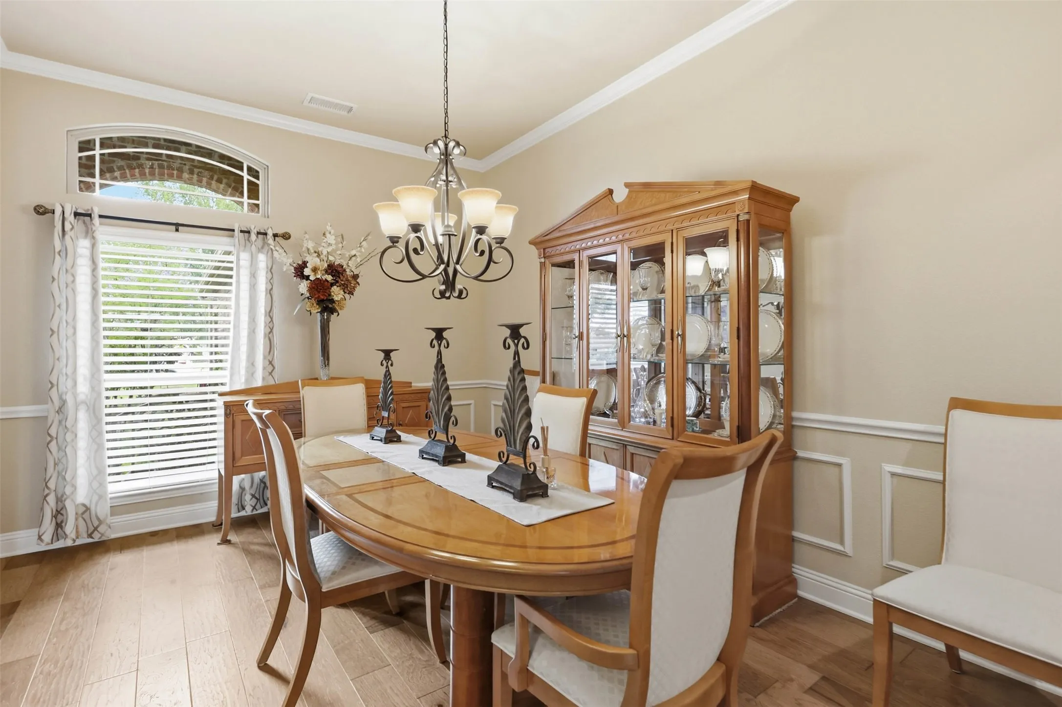 Formal dining space featuring wood-finish flooring, a decorative chandelier, crown molding, and wainscoting