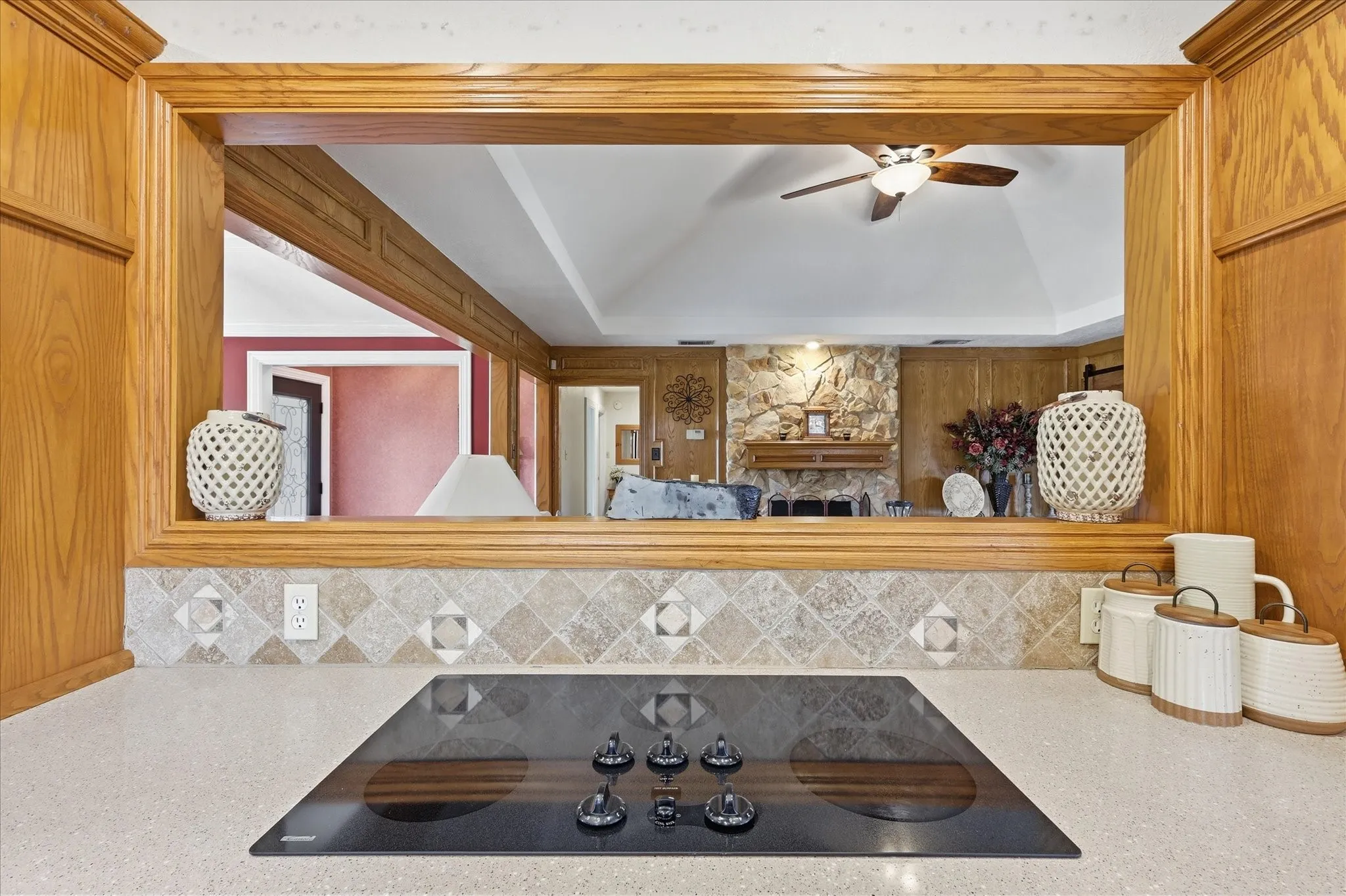 Kitchen counter with an integrated black glass cooktop, stone-look tiled backsplash, and light-toned countertop