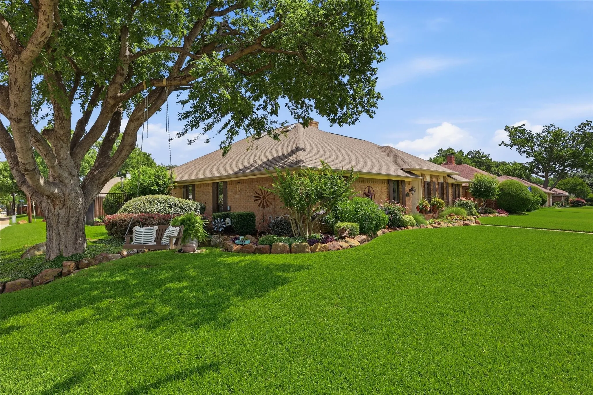 Brick exterior residence with a sloped roofline, featuring a verdant lawn, mature trees, and established shrubbery