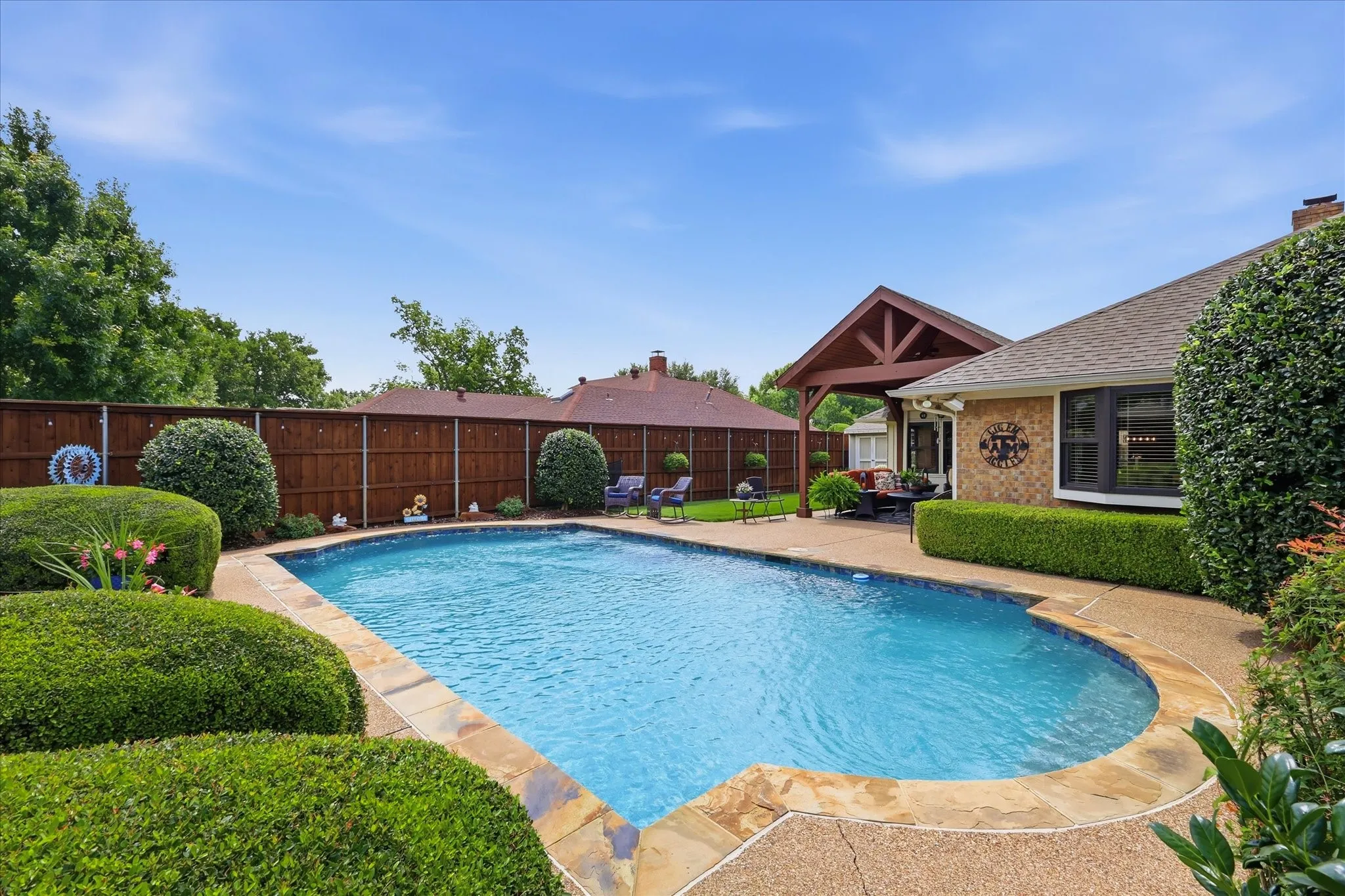 Resort-style backyard featuring a freeform swimming pool with stone coping, a spacious patio area, a wood pergola, and mature landscaping