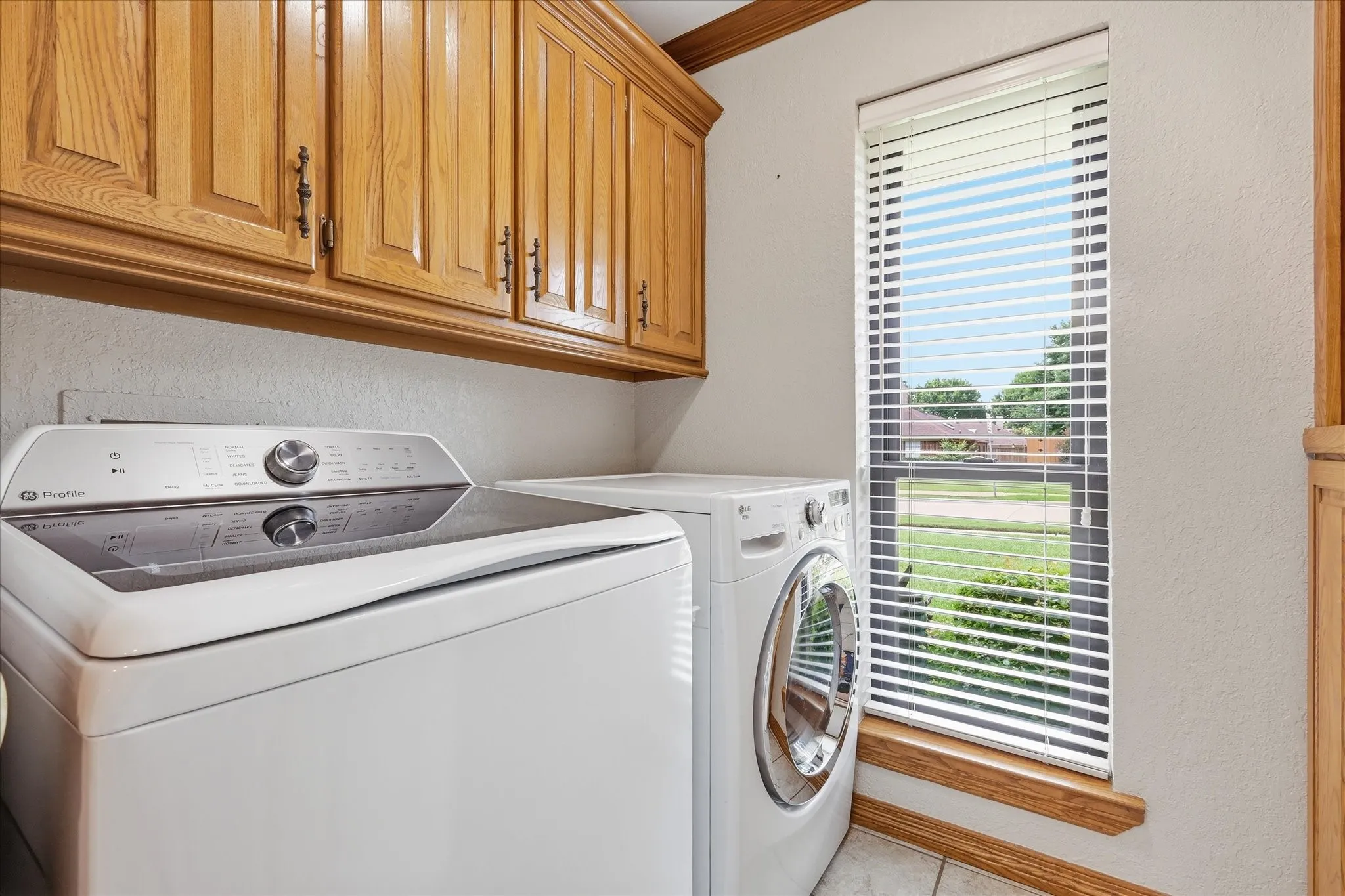 Dedicated laundry area featuring wood cabinetry, a large window with blinds, and tile flooring