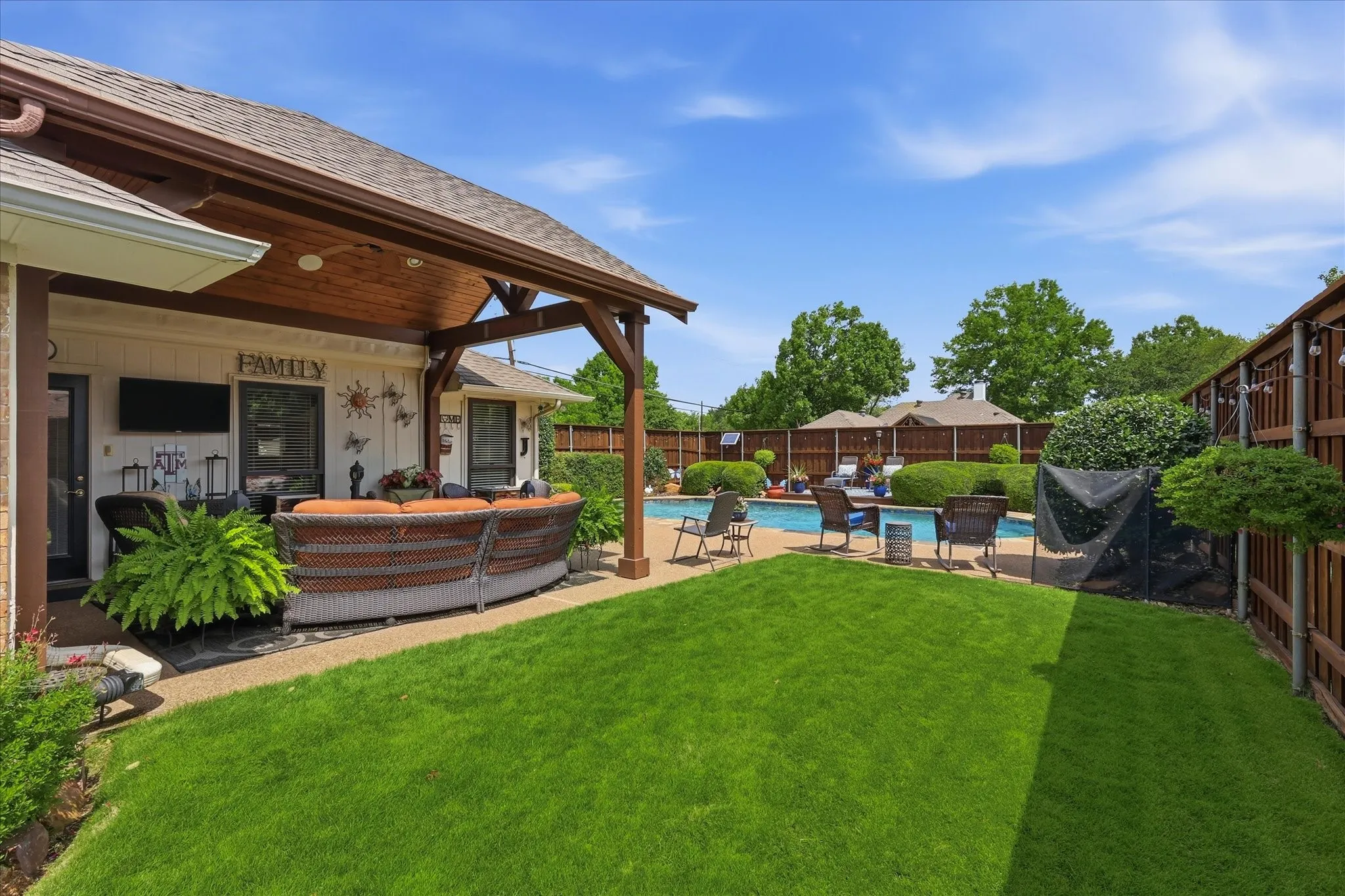 Expansive backyard with covered patio, manicured lawn, and inground swimming pool
