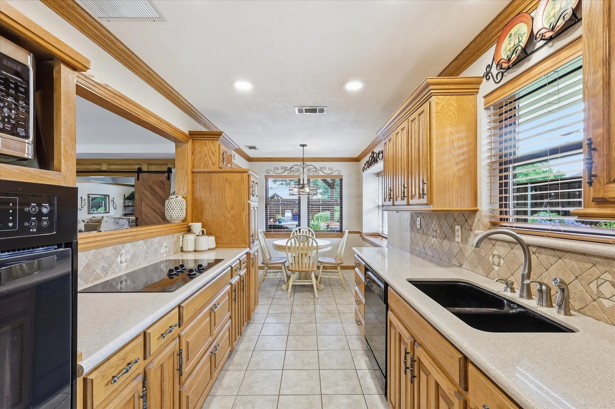 Galley kitchen featuring light wood cabinetry, light countertops, an electric cooktop, and a double basin sink