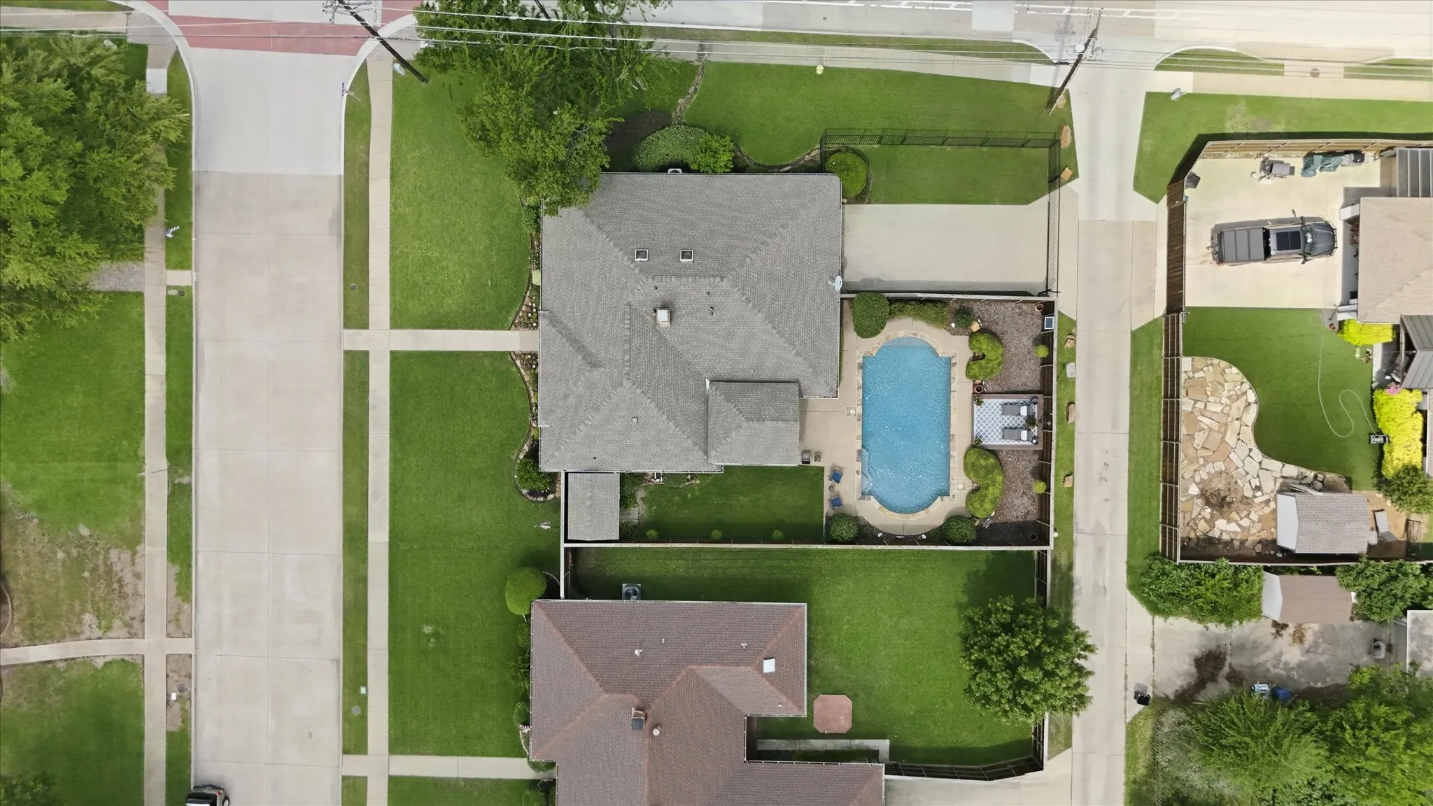 Aerial perspective showcasing a property with a fenced backyard featuring a freeform swimming pool, surrounding paved patio, and mature landscaping