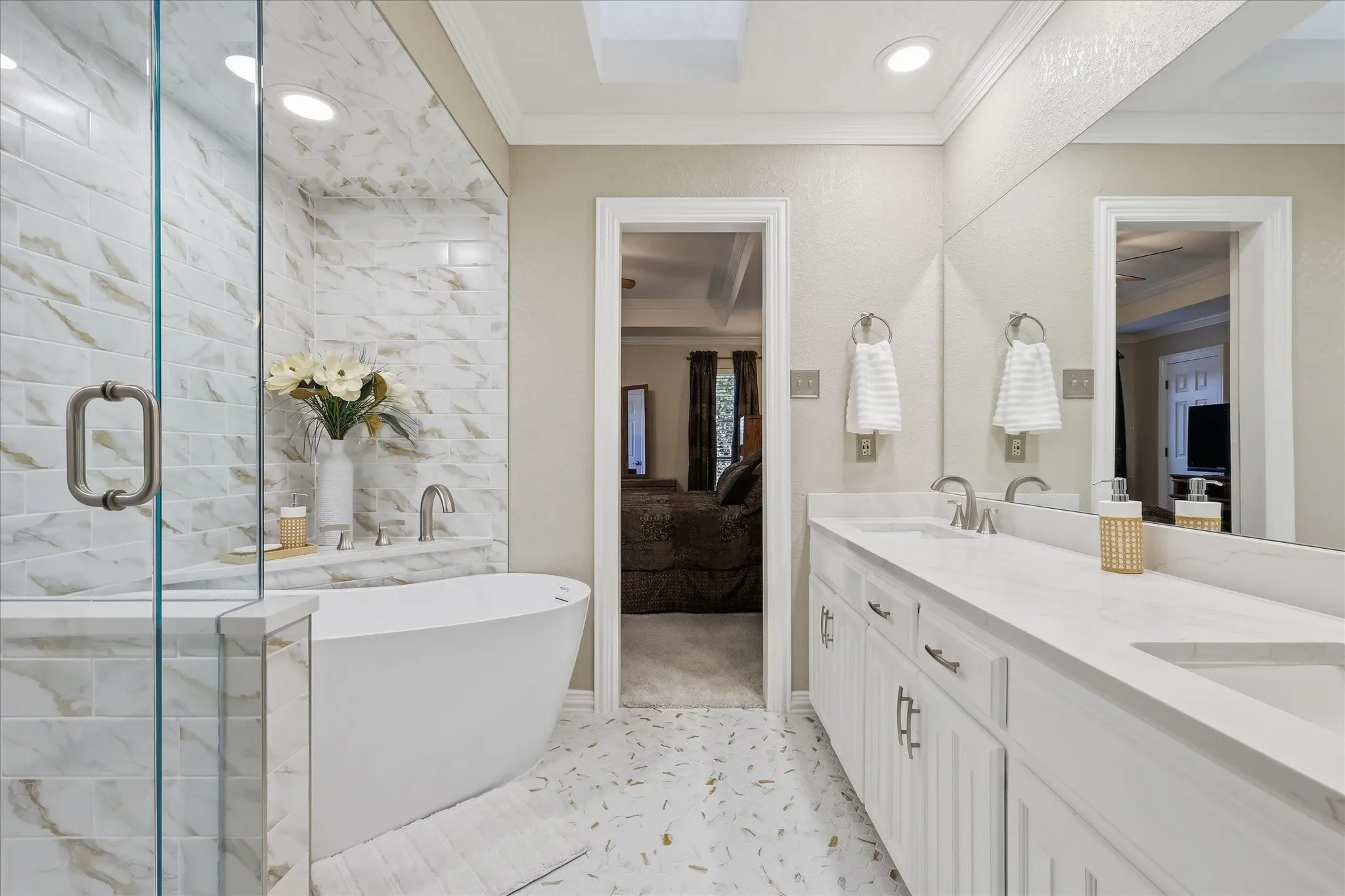 Freestanding soaking tub with a tiled accent wall, glass-enclosed shower, dual vanity with undermount sinks, and a full-width mirror