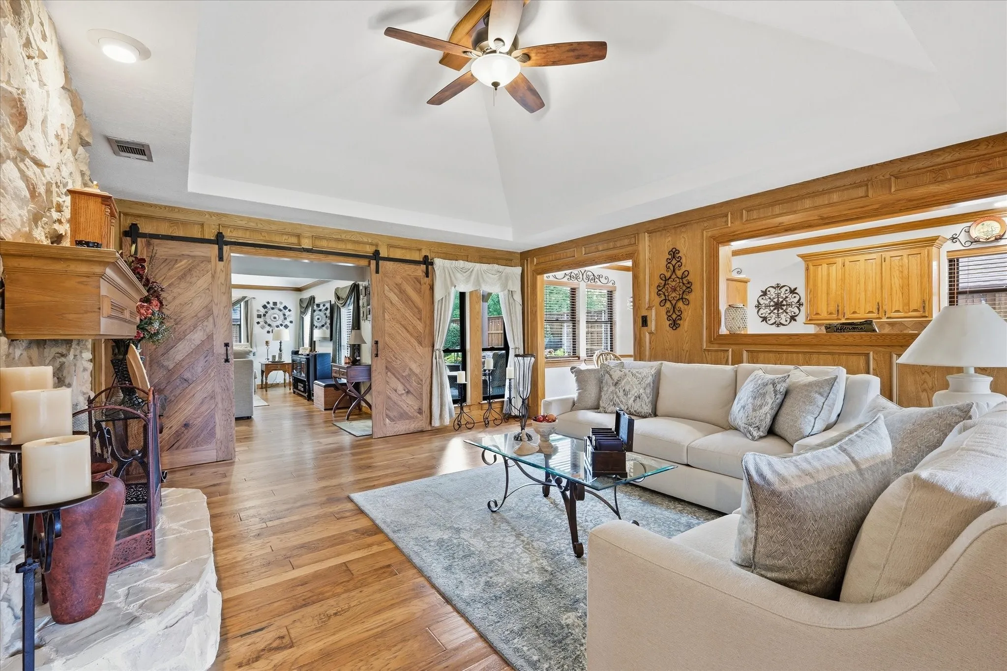 Vaulted ceiling living area featuring wood-finish flooring, a stone fireplace with a wood mantle, and decorative wood​​‌​​​​‌​​‌‌​‌‌​​​‌‌​‌​‌​‌​​​‌​​ paneling