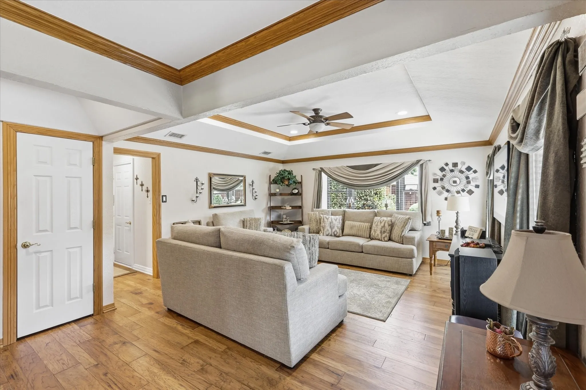 Spacious living area featuring wood-finish flooring, a tray ceiling with recessed lighting and a ceiling fan, and prominent wood trim accents