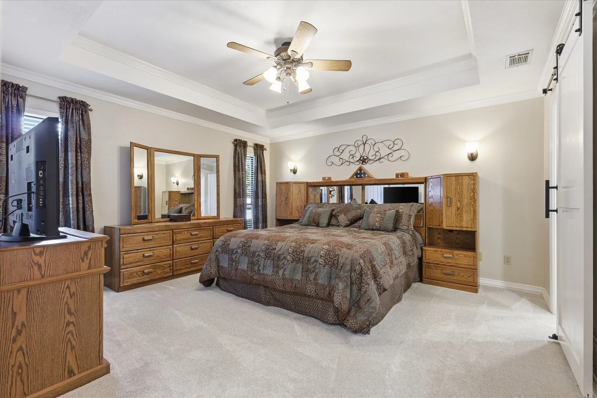 Spacious room featuring tray ceilings, neutral wall paint, and light-toned carpet flooring