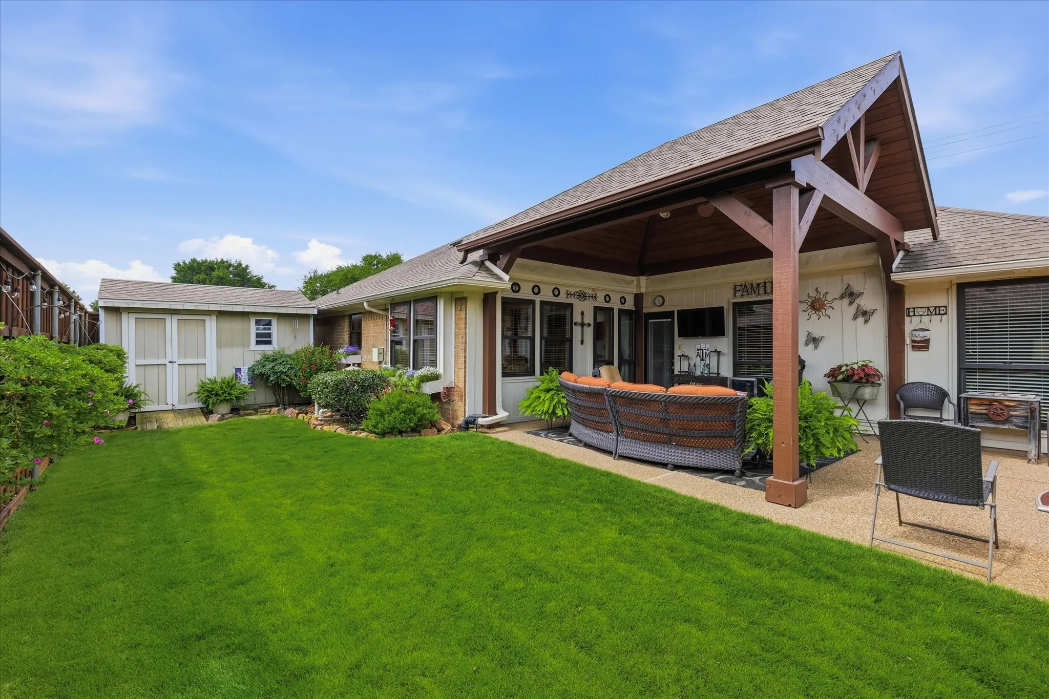 Expansive backyard featuring a manicured lawn, a gravel patio, and a covered outdoor living area with exposed wood beams