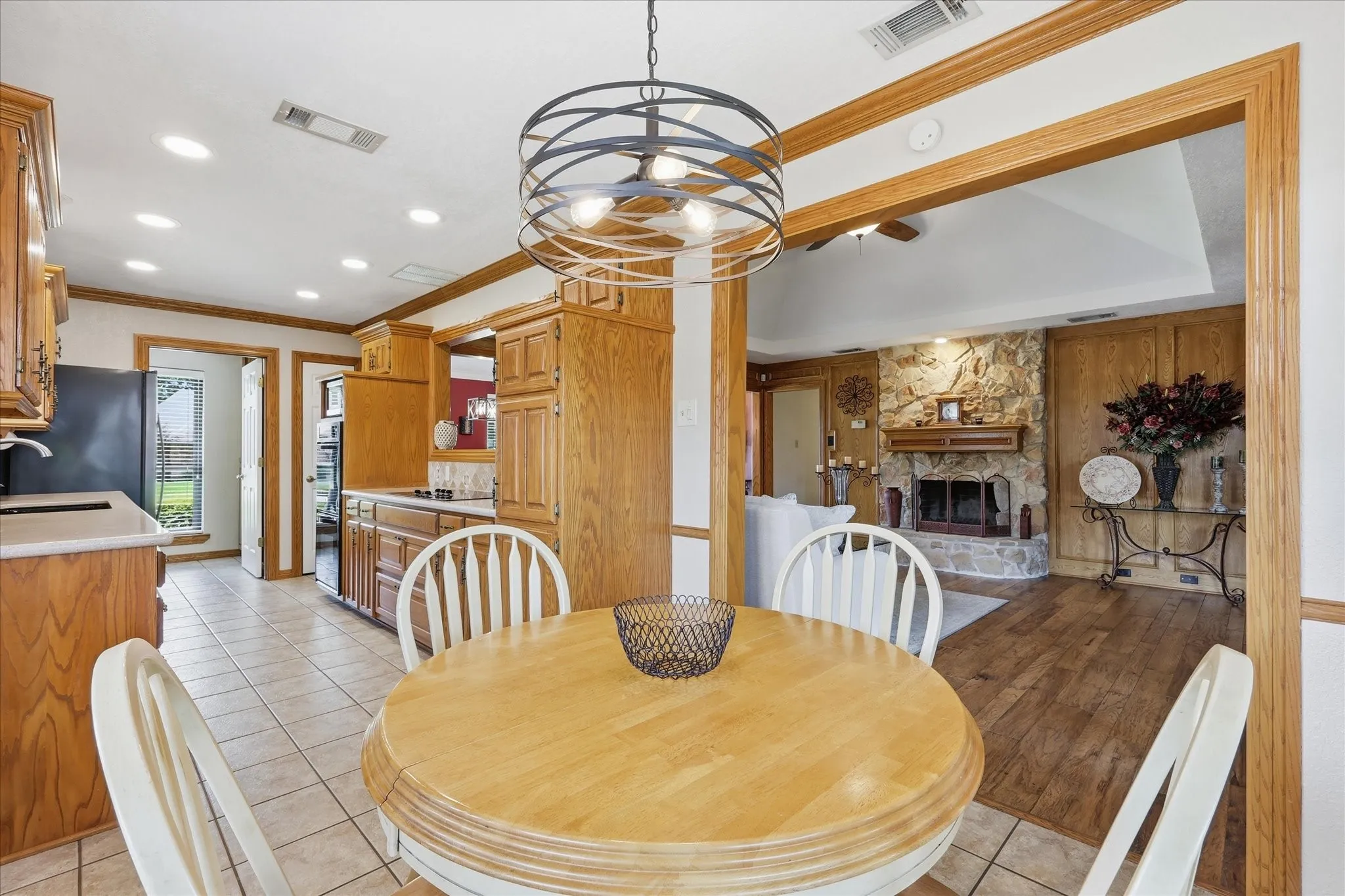 Open-concept dining area featuring a circular wood-finish table, tile flooring, and a contemporary chandelier