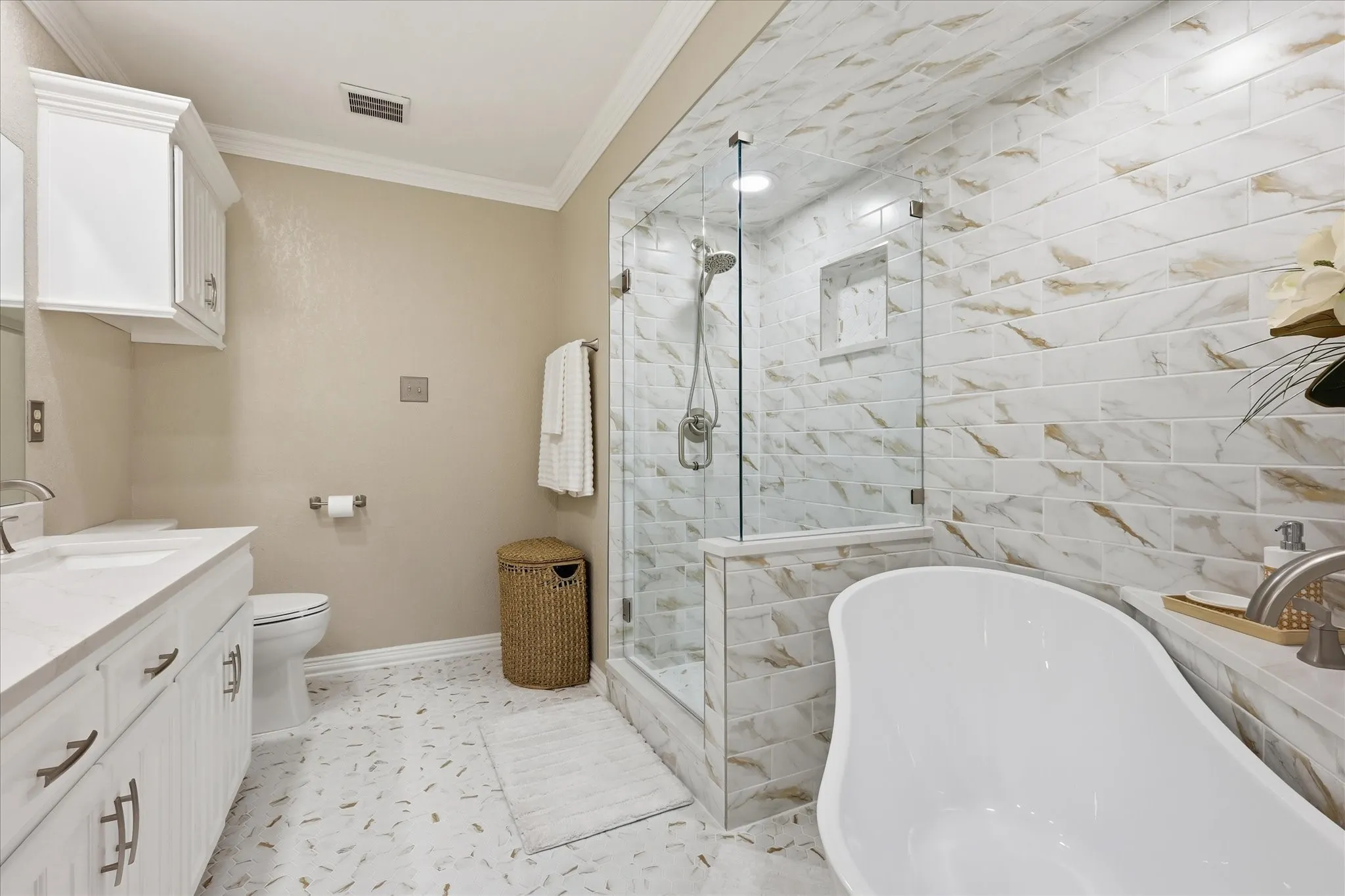 Bathroom featuring a freestanding soaking tub, glass-enclosed shower with subway tile surround, double vanity with white cabinetry and integrated sinks, and crown molding