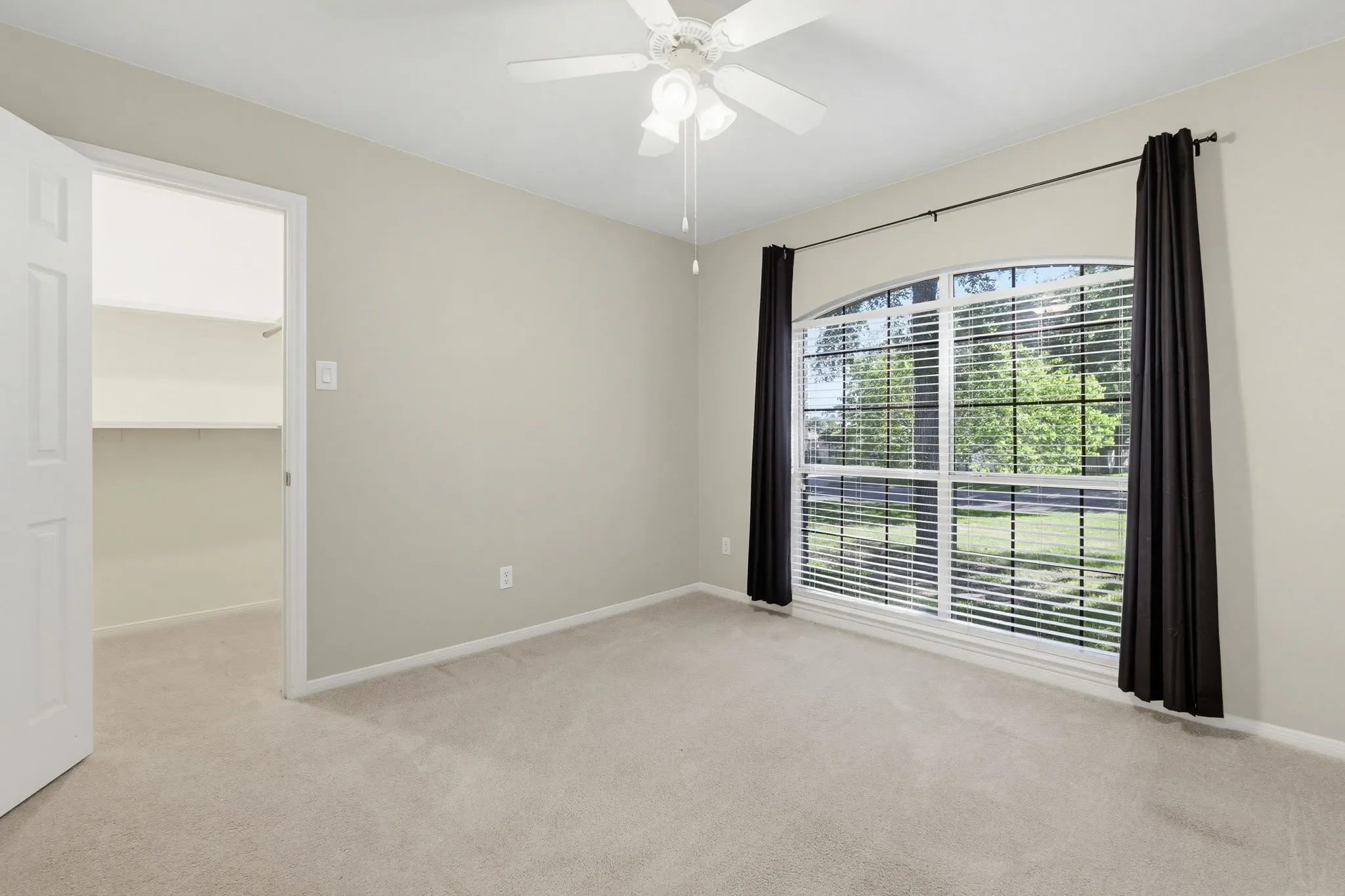 Neutral-toned room featuring an arched window, soft carpet flooring, and a ceiling fan