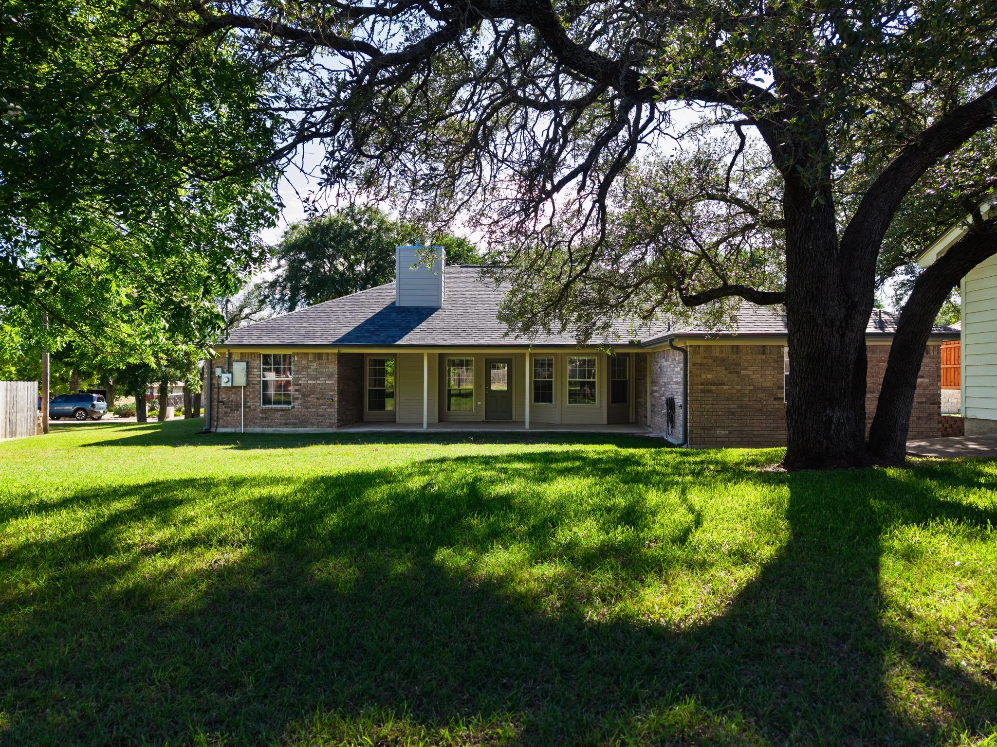 Rear exterior featuring a covered patio, brick construction, multiple windows, and a shingle roof with a chimney