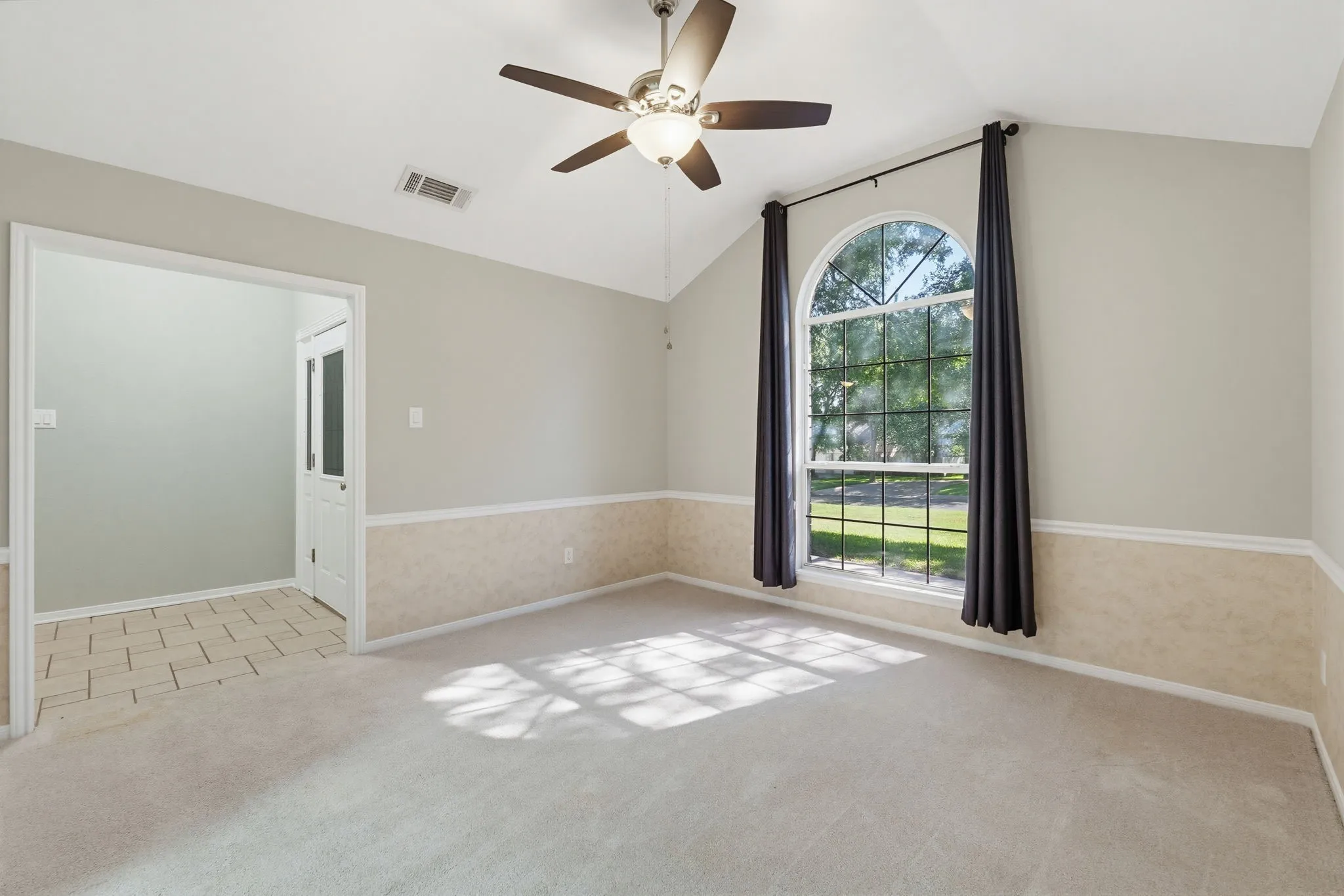 Vaulted ceiling room featuring an arched window, ceiling fan, and carpeted flooring