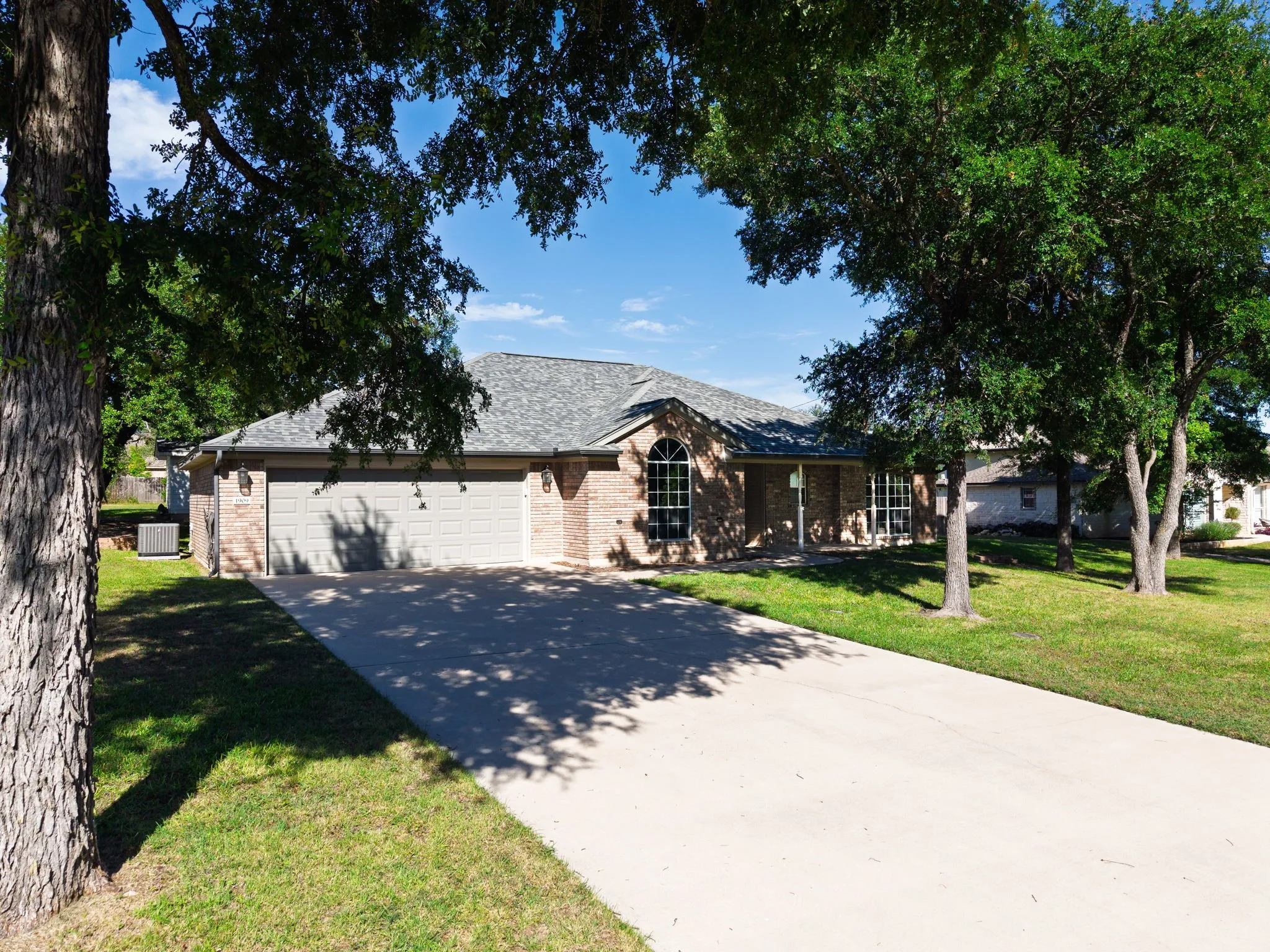 Brick facade home featuring a two-car garage with individual doors, a concrete driveway, and mature landscaping