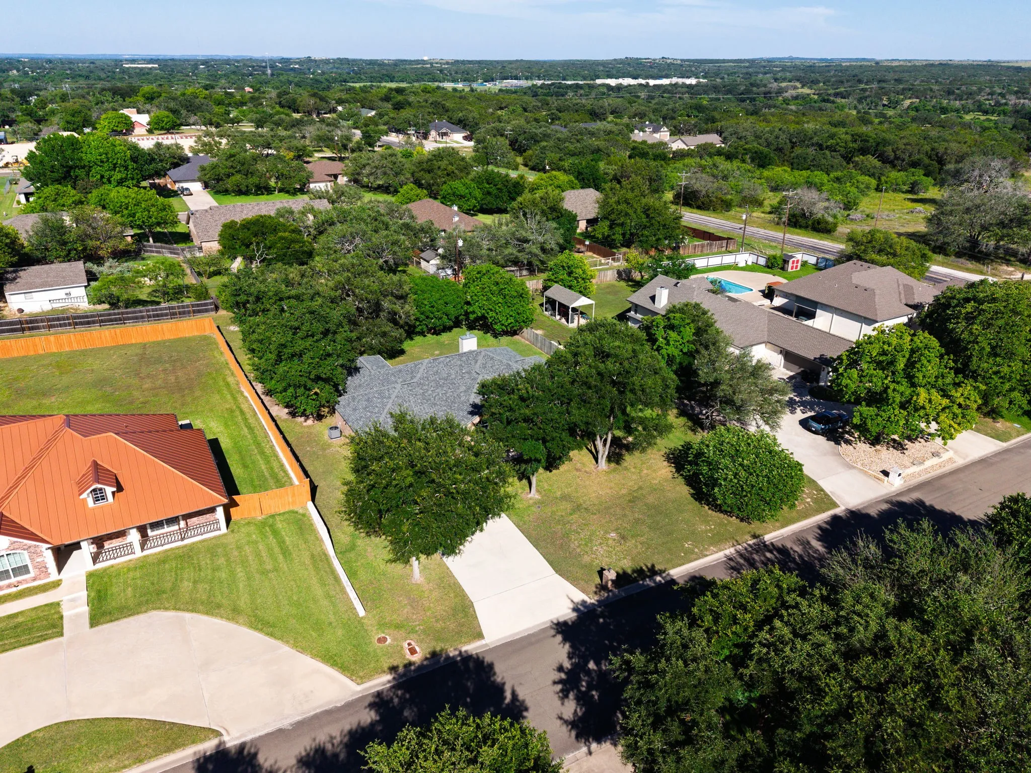 Residential property featuring a swimming pool, mature trees, a paved driveway, and a fenced yard