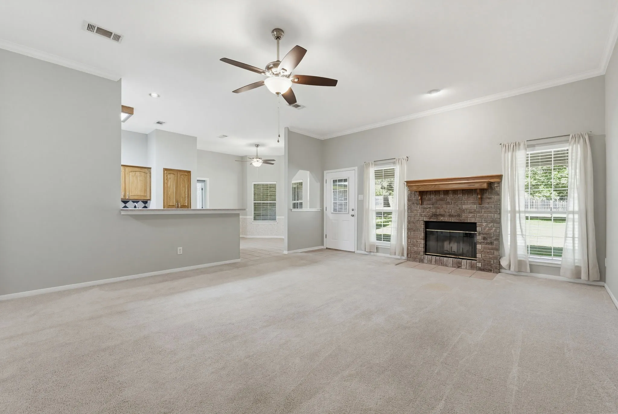 Spacious living area featuring neutral carpeting, a brick fireplace with a wood mantel, and multiple windows