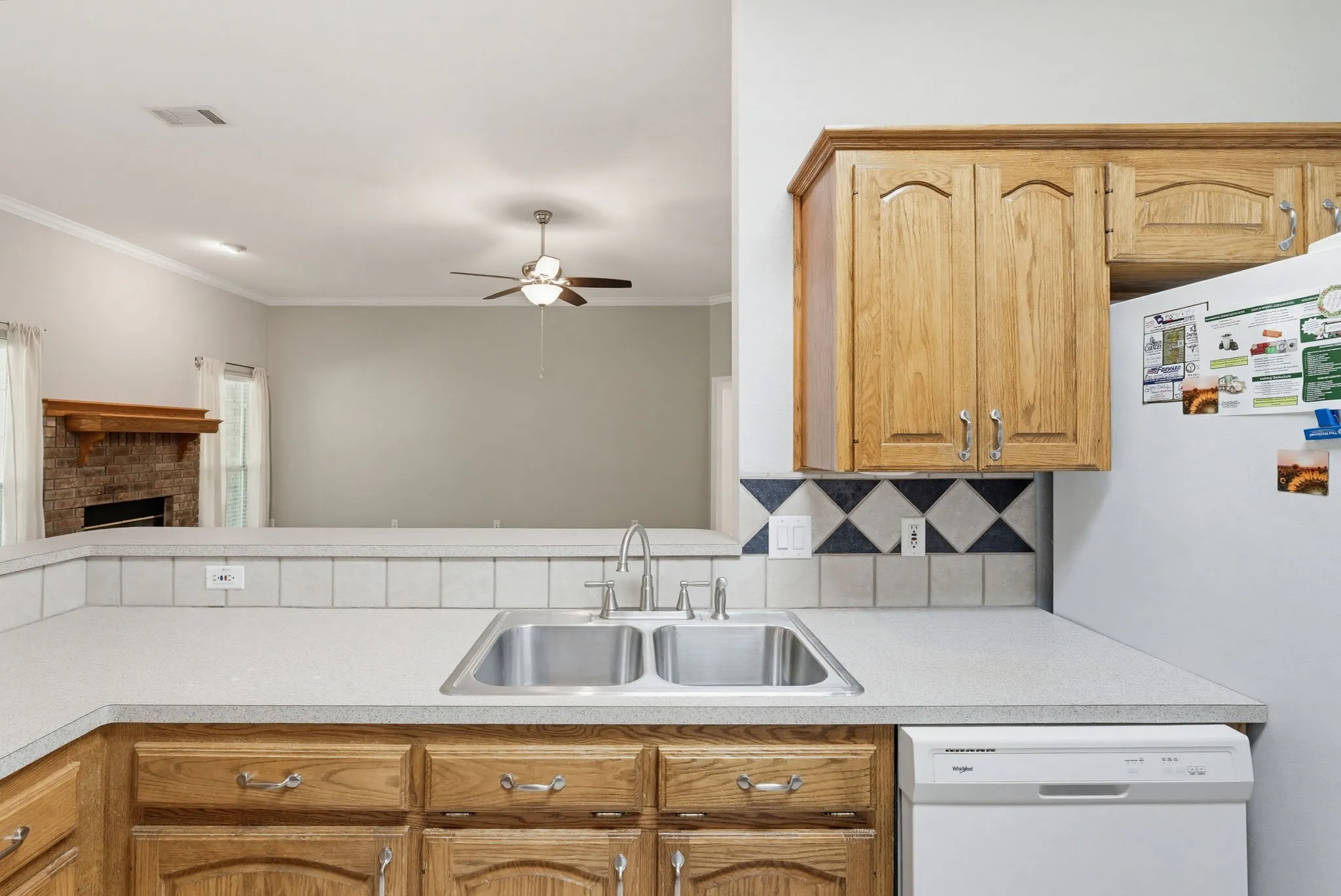 Kitchen featuring light wood cabinetry, a double basin stainless steel sink with a gooseneck faucet, light countertops, and a patterned tile backsplash