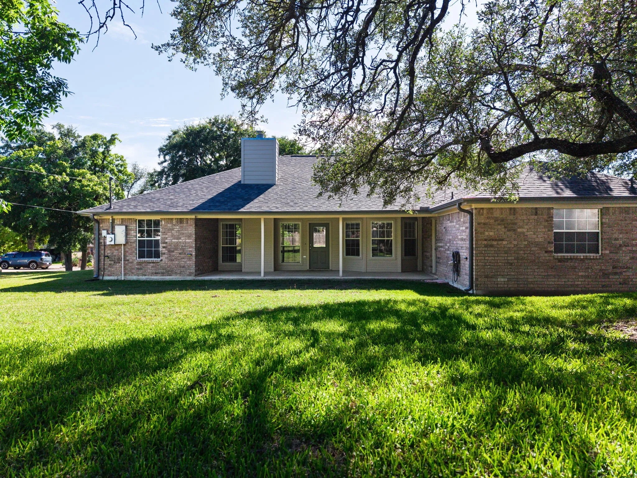 Expansive backyard with a manicured lawn, mature trees, and a covered patio