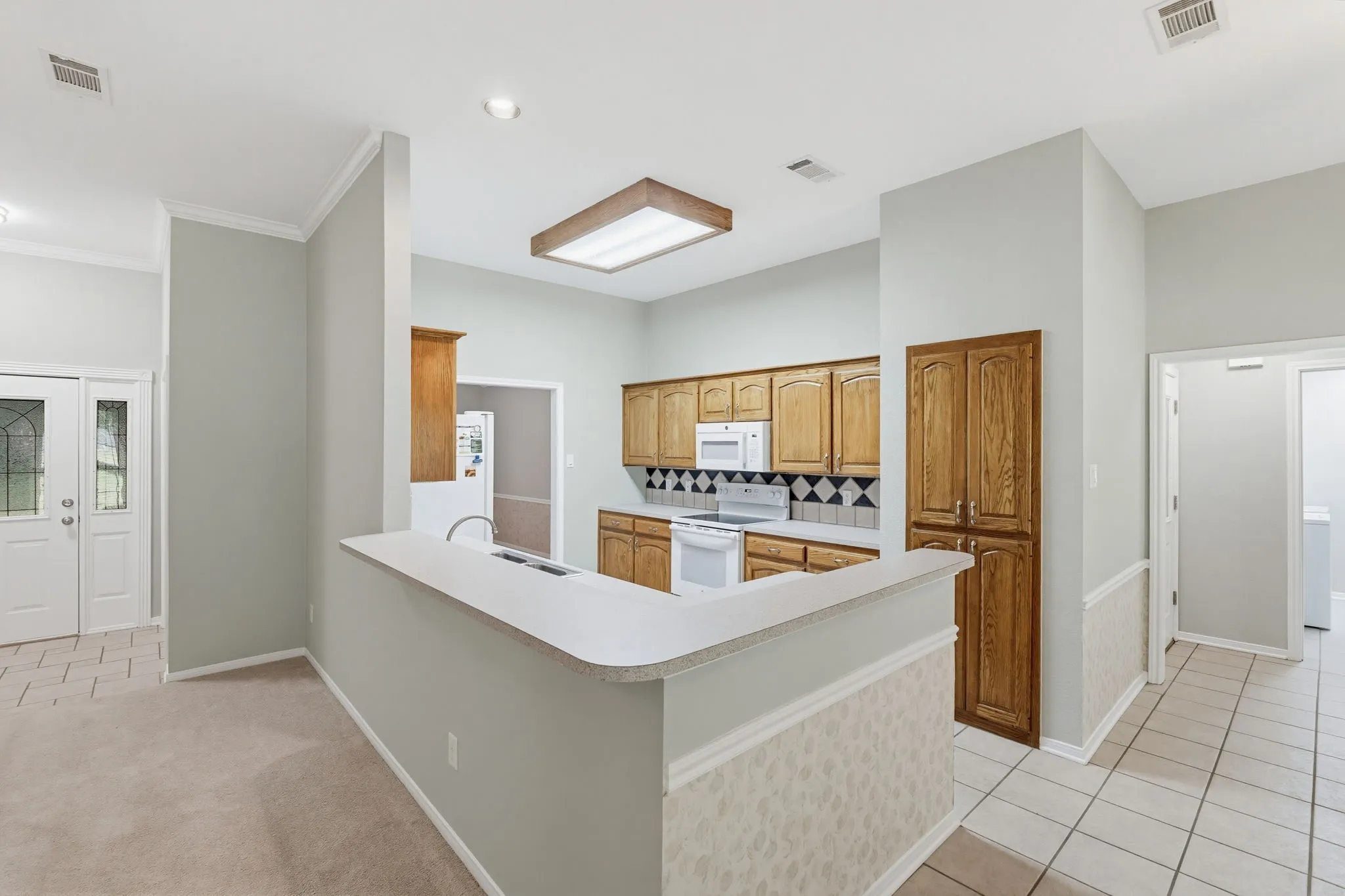 Kitchen with white appliances, wood cabinetry, and a peninsula countertop