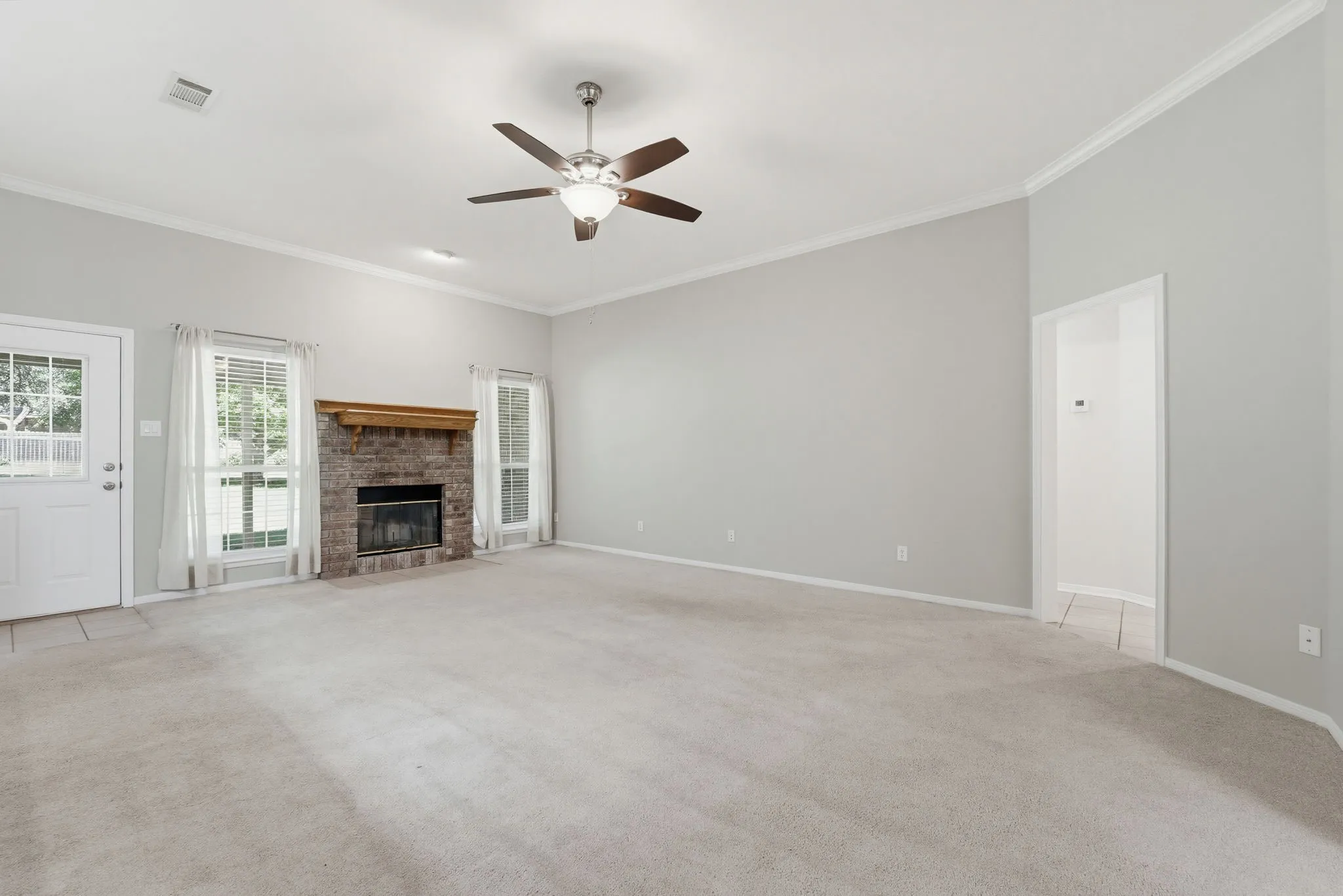 Spacious living area featuring a brick fireplace with a wood mantel, light gray wall paint, and white trim