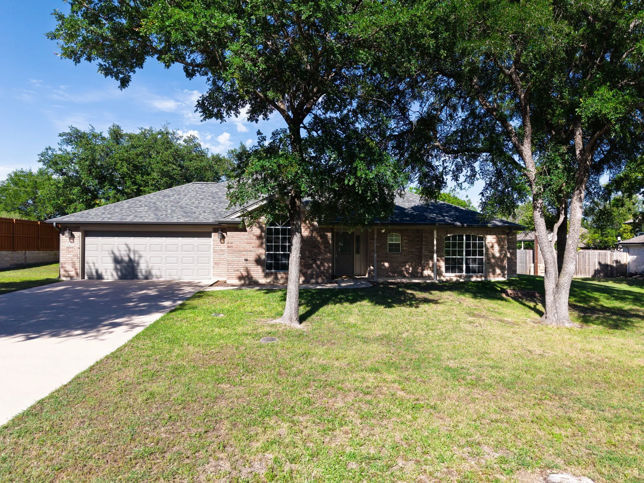 Brick exterior featuring a two-car garage, concrete driveway, and established trees