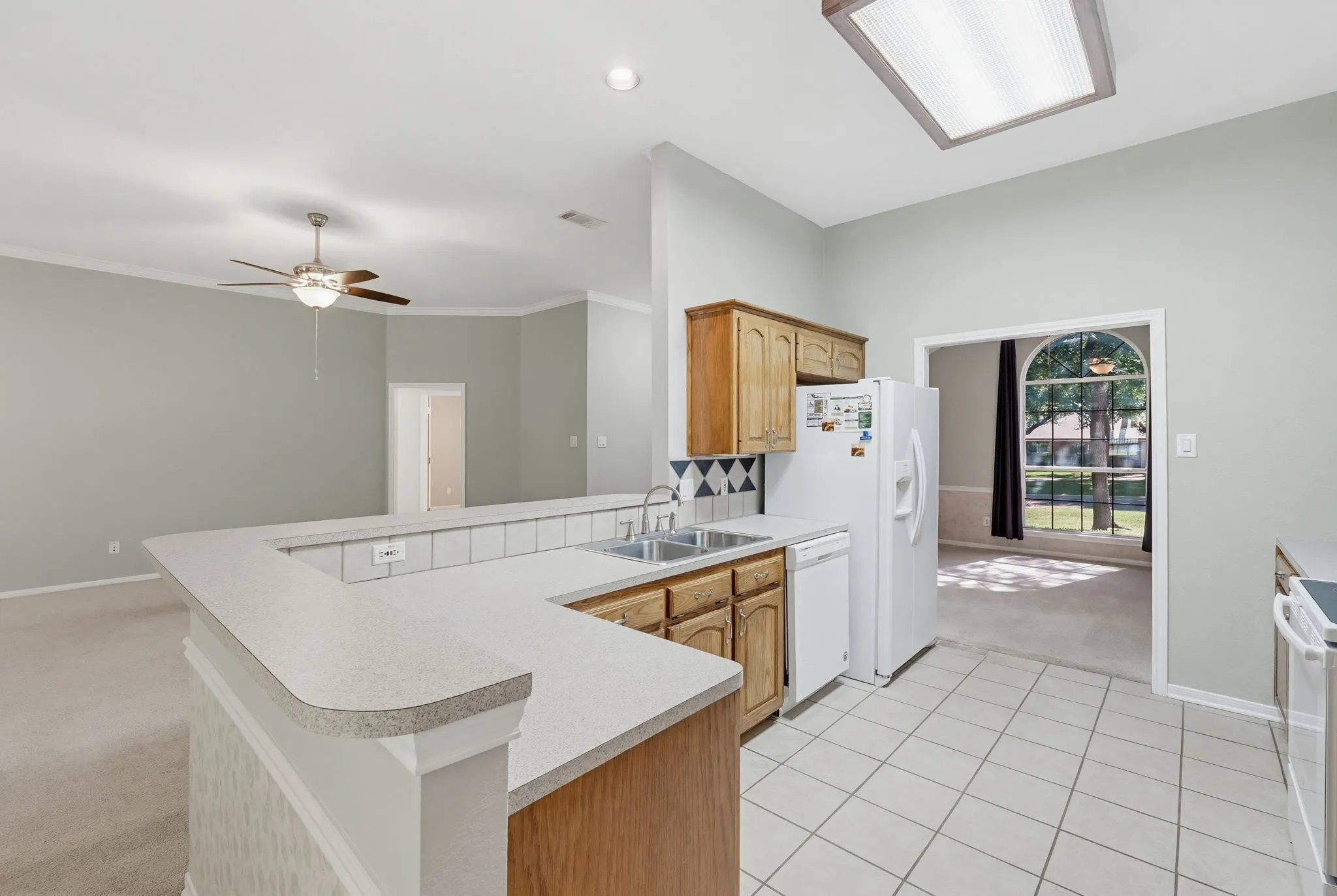 Kitchen featuring a breakfast bar with laminate countertops, light wood cabinetry, and white tile flooring