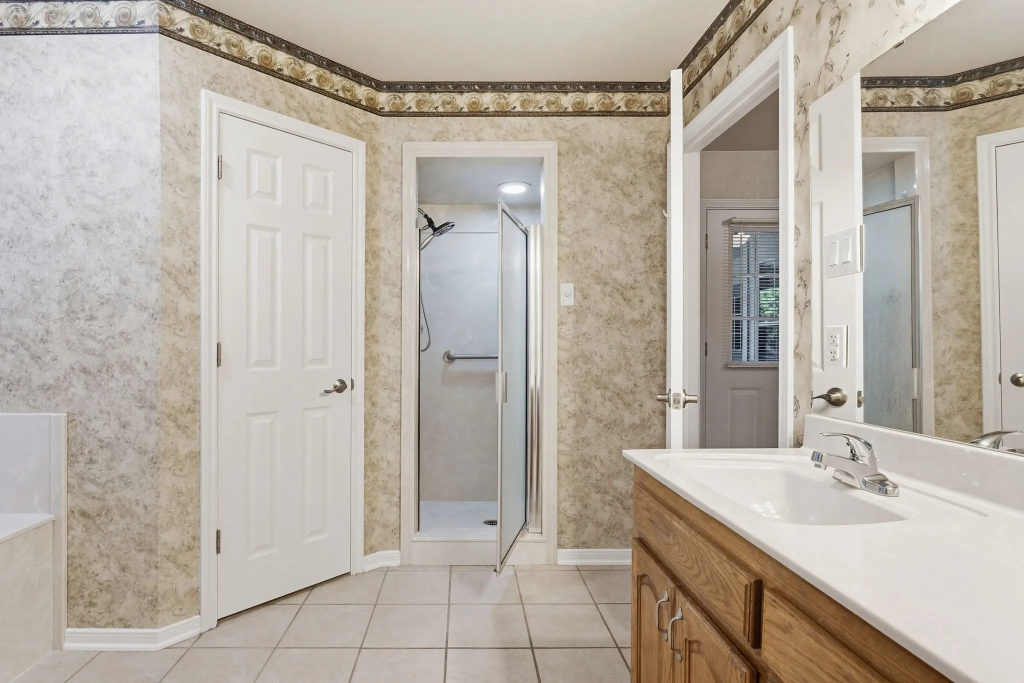 Bathroom featuring tiled flooring, a glass-enclosed shower, a built-in vanity with a white countertop and integrated sink, and an overhead lighting fixture
